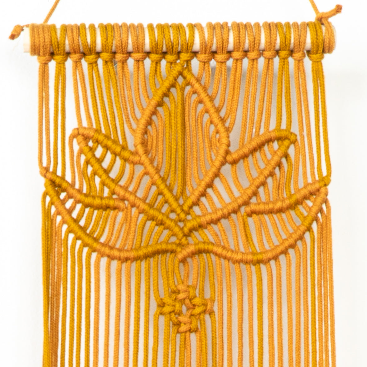 Yellow macrame wall hanging with a leaf design on a white background