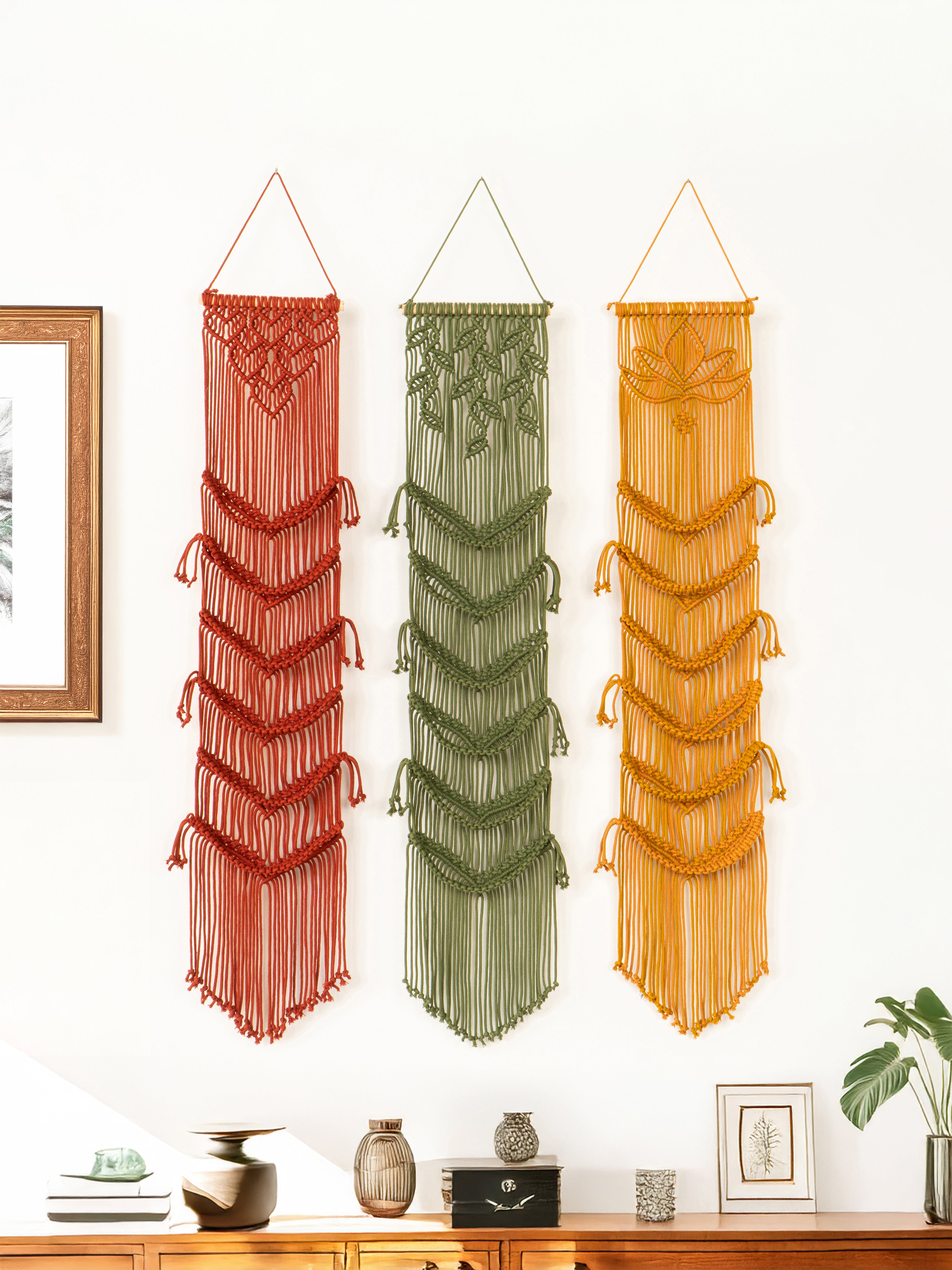 Three string wall hangings in red, green, and orange on a white wall.