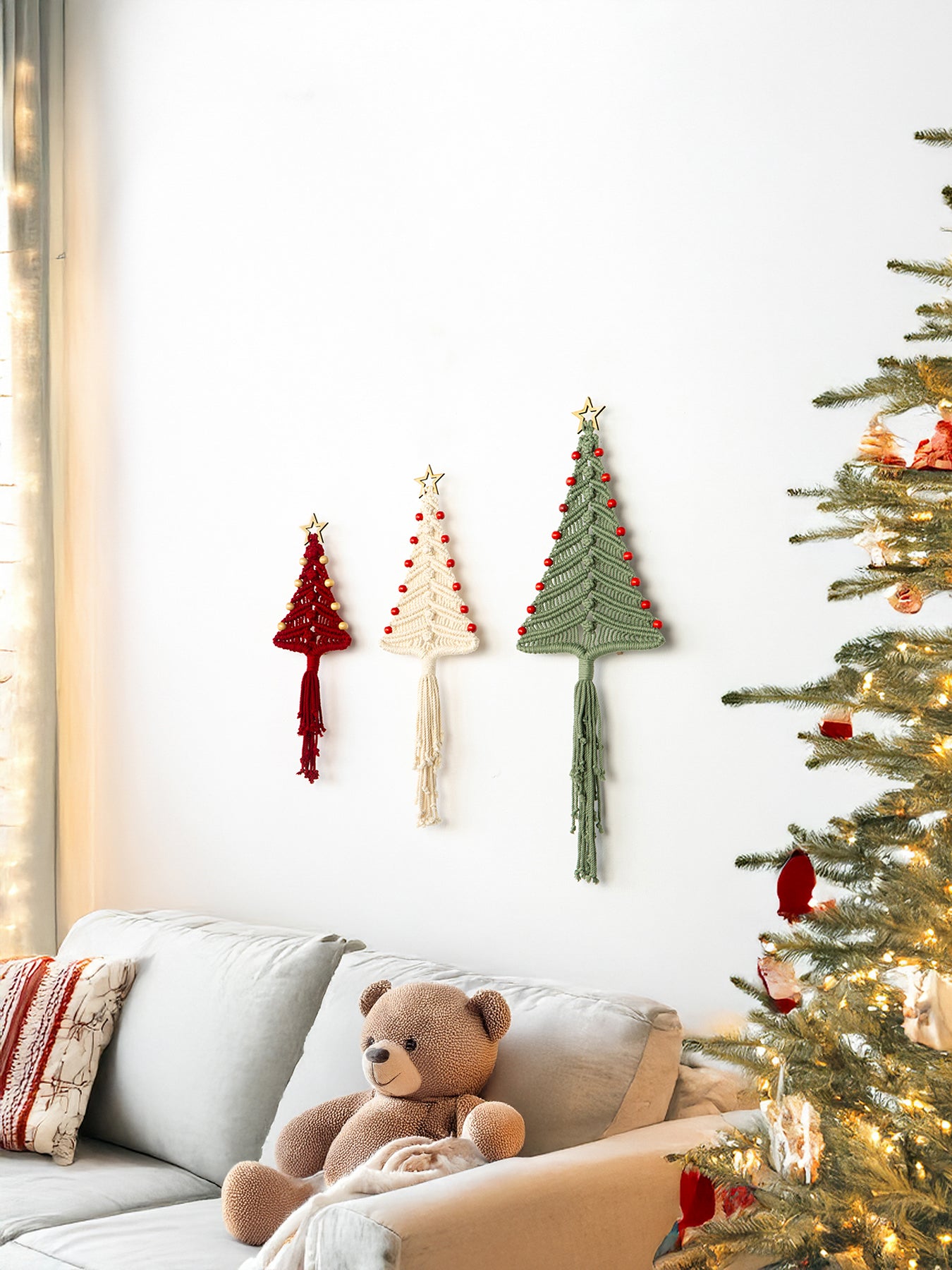 Decorative Christmas trees on a wall with a teddy bear on a couch and a lit Christmas tree in the corner.
