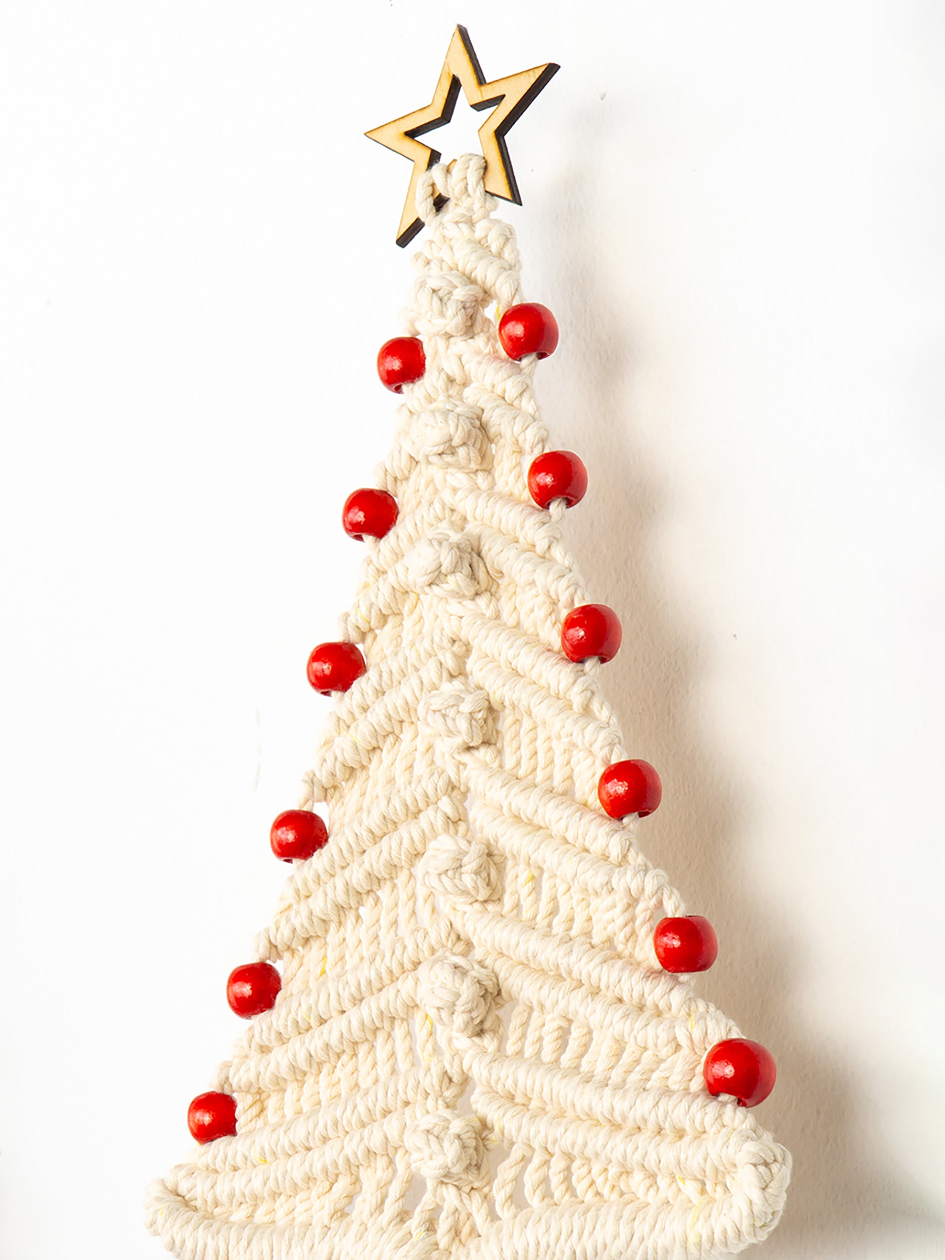 Knitted Christmas tree ornament with red berries and a gold star on a white background