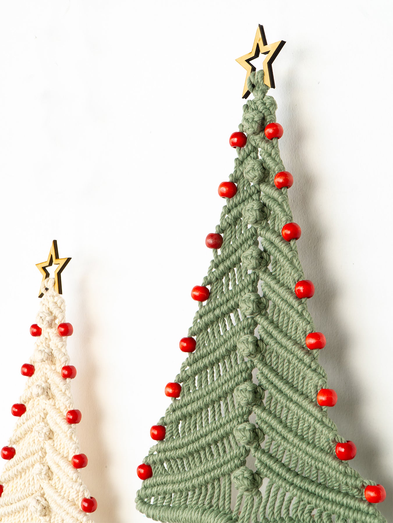 Two macrame Christmas trees, one green and one beige, with red beads and gold stars on a white background.