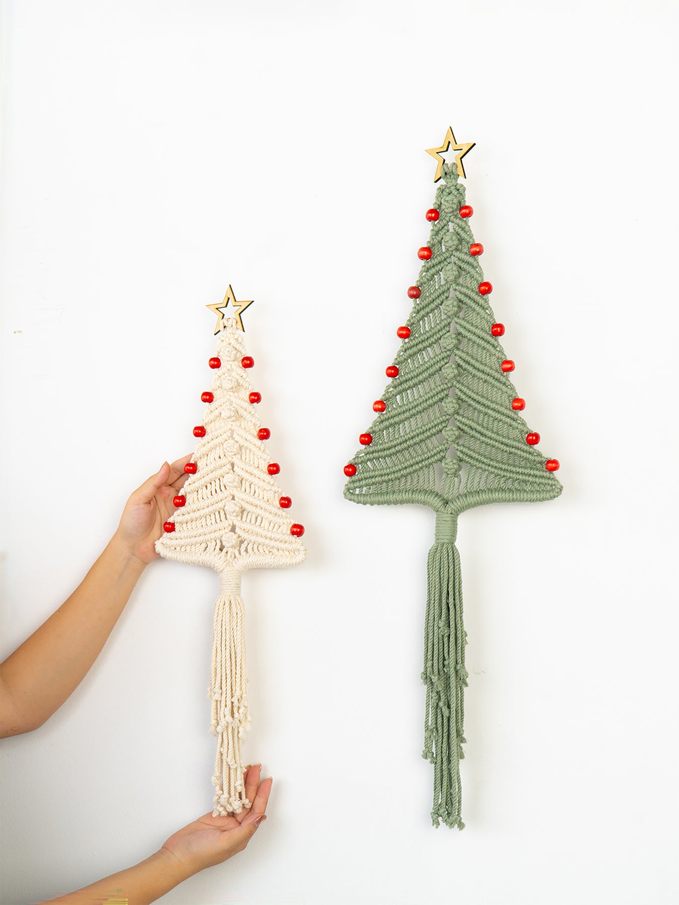 Two macrame Christmas tree wall hangings, one beige and one green, on a white background.