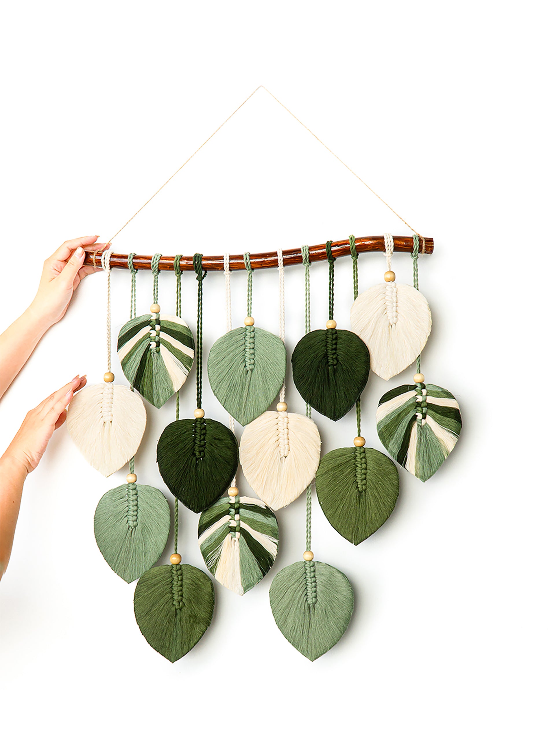 Colorful leaf-shaped wall hanging with a hand reaching to adjust it on a white background