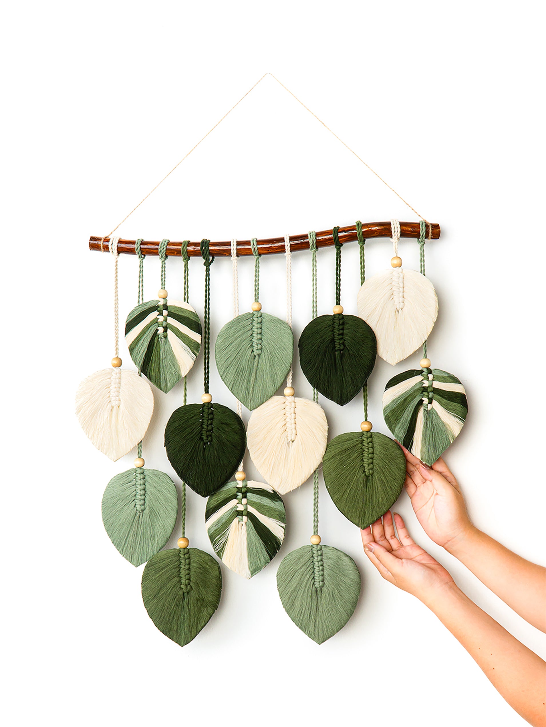 Handmade wall hanging with leaf-shaped green and beige fabric pieces on a white background