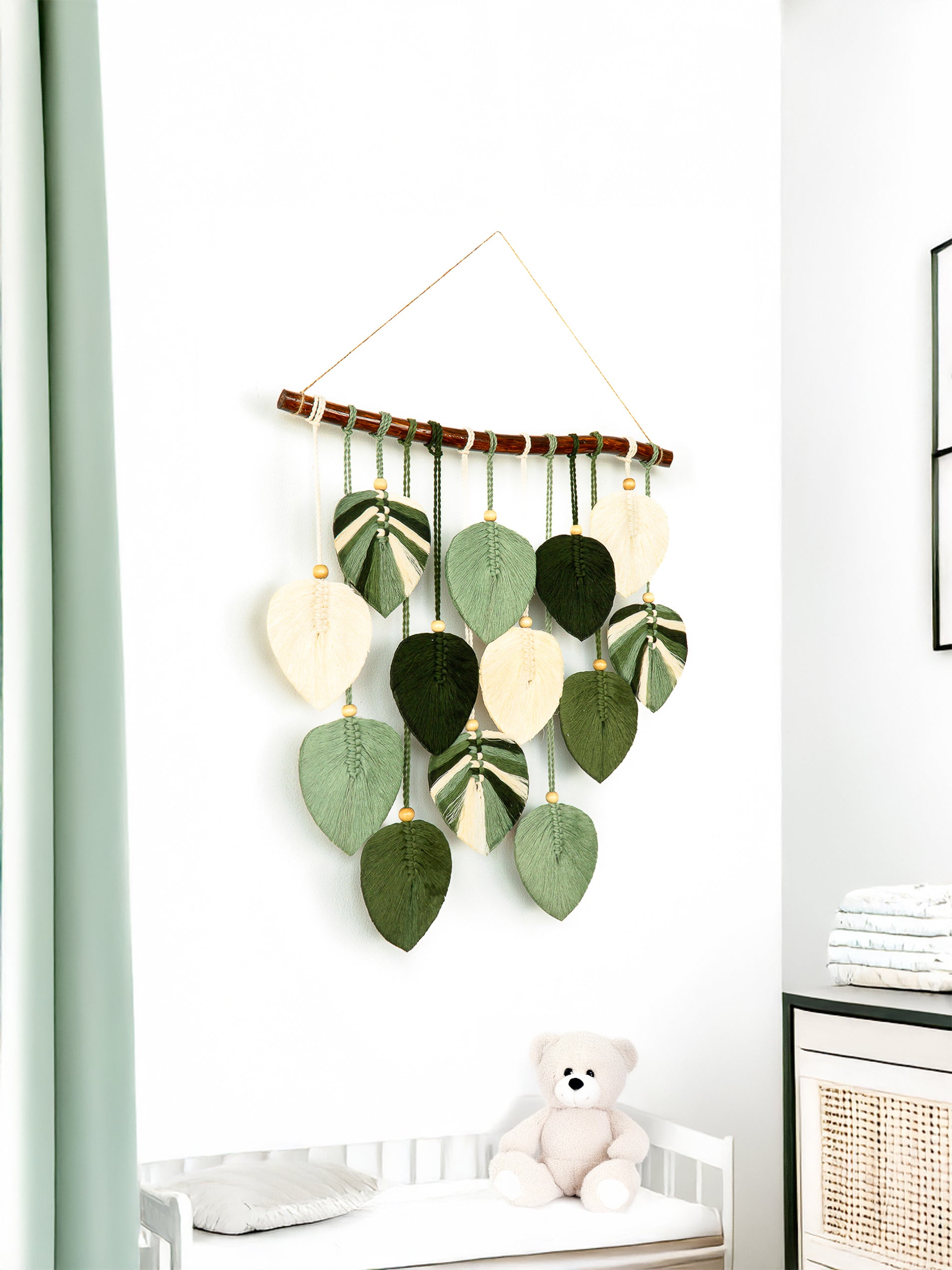 Decorative wall hanging with green and white leaves in a room with a teddy bear and a radiator.