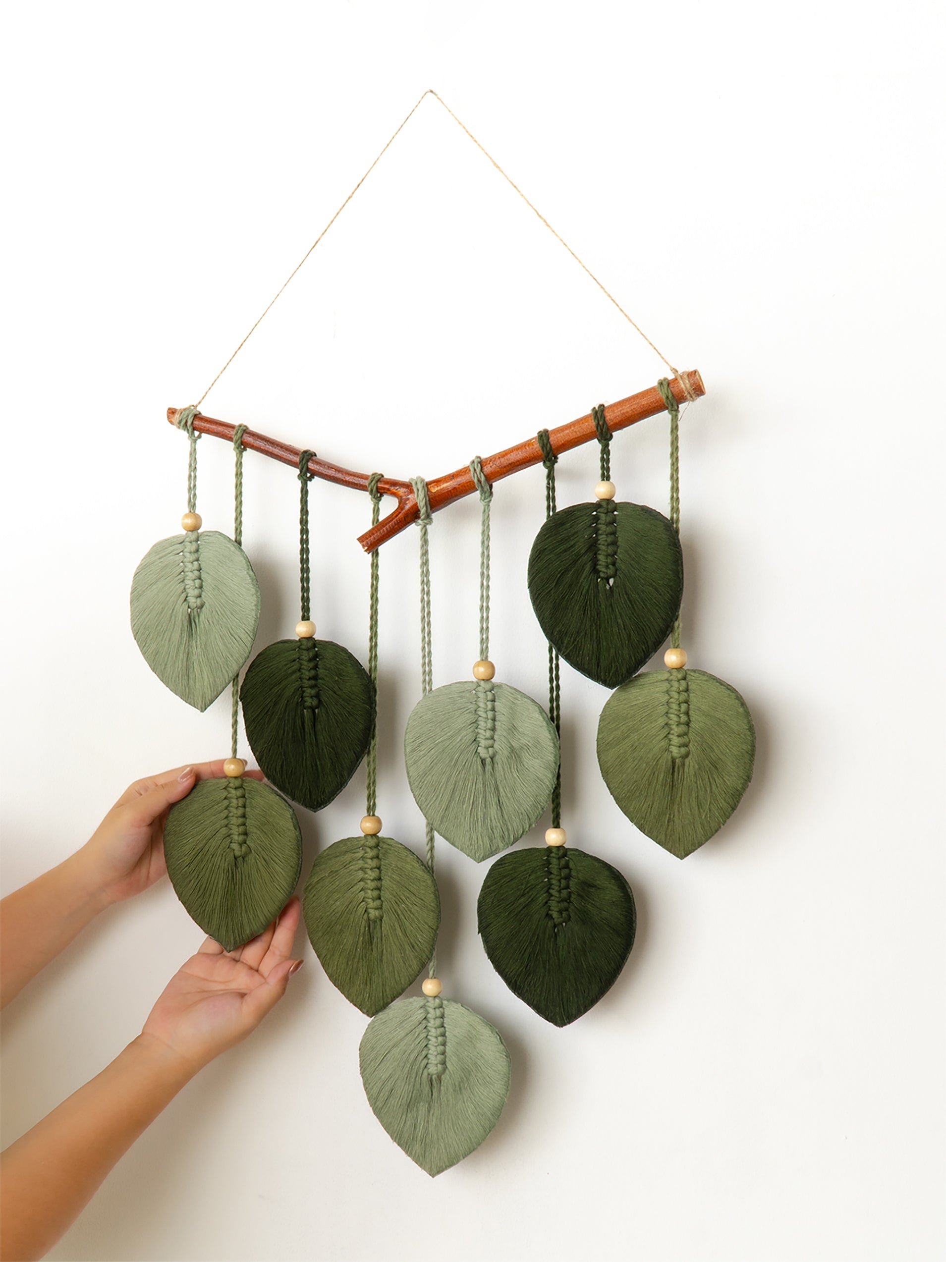 Handmade wall hanging with leaf-shaped green fabric pieces on a white background