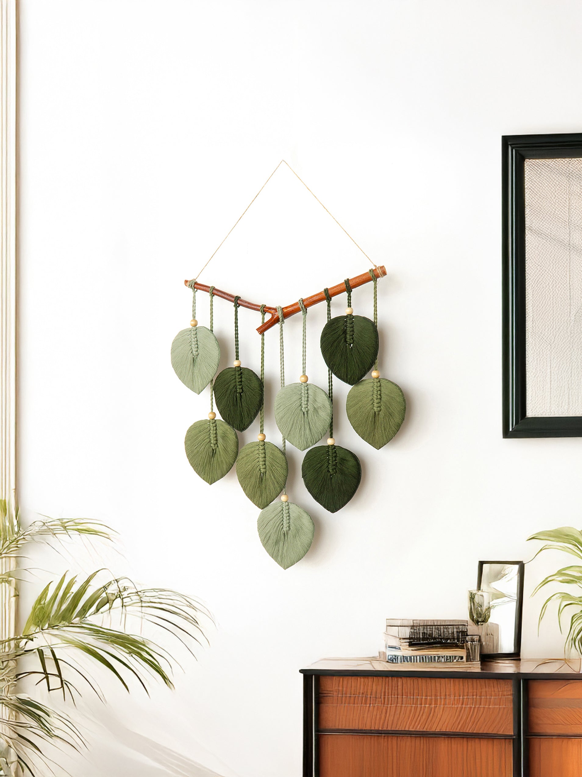 Decorative wall hanging with leaf-shaped green elements on a white wall.