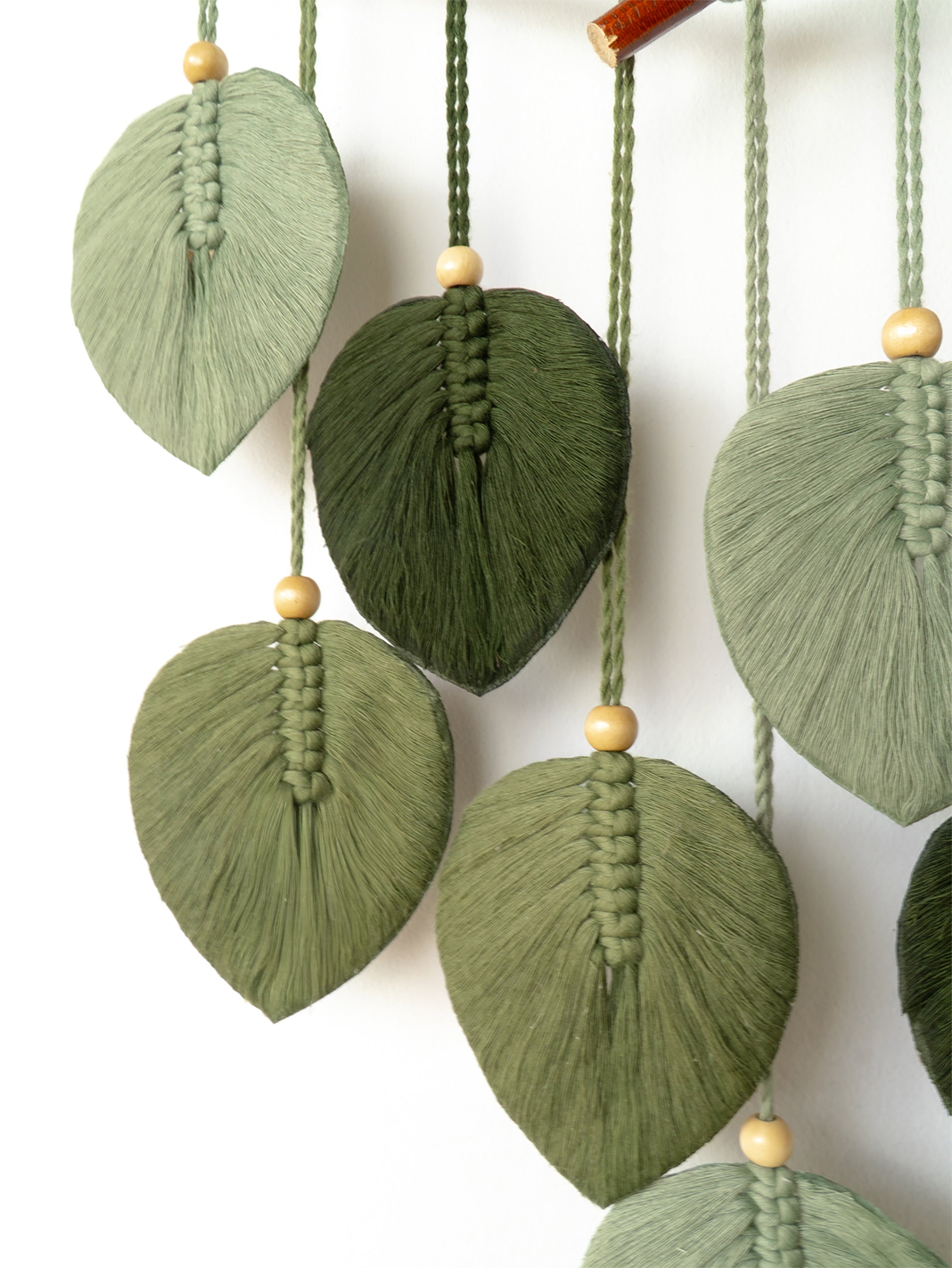 Colorful yarn leaf decorations hanging from a branch against a white background
