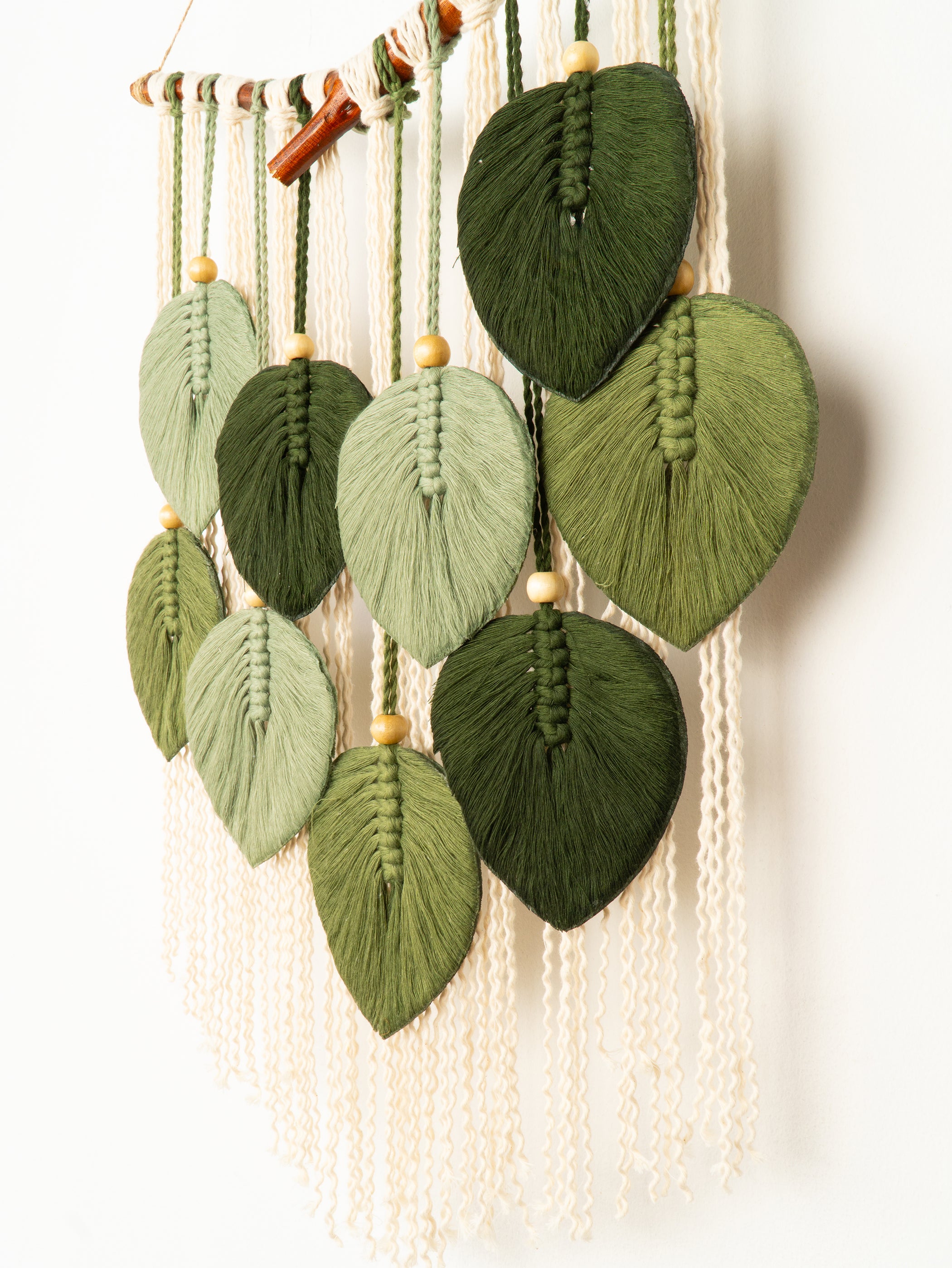 Macrame wall hanging with green leaf-shaped knots on a white background