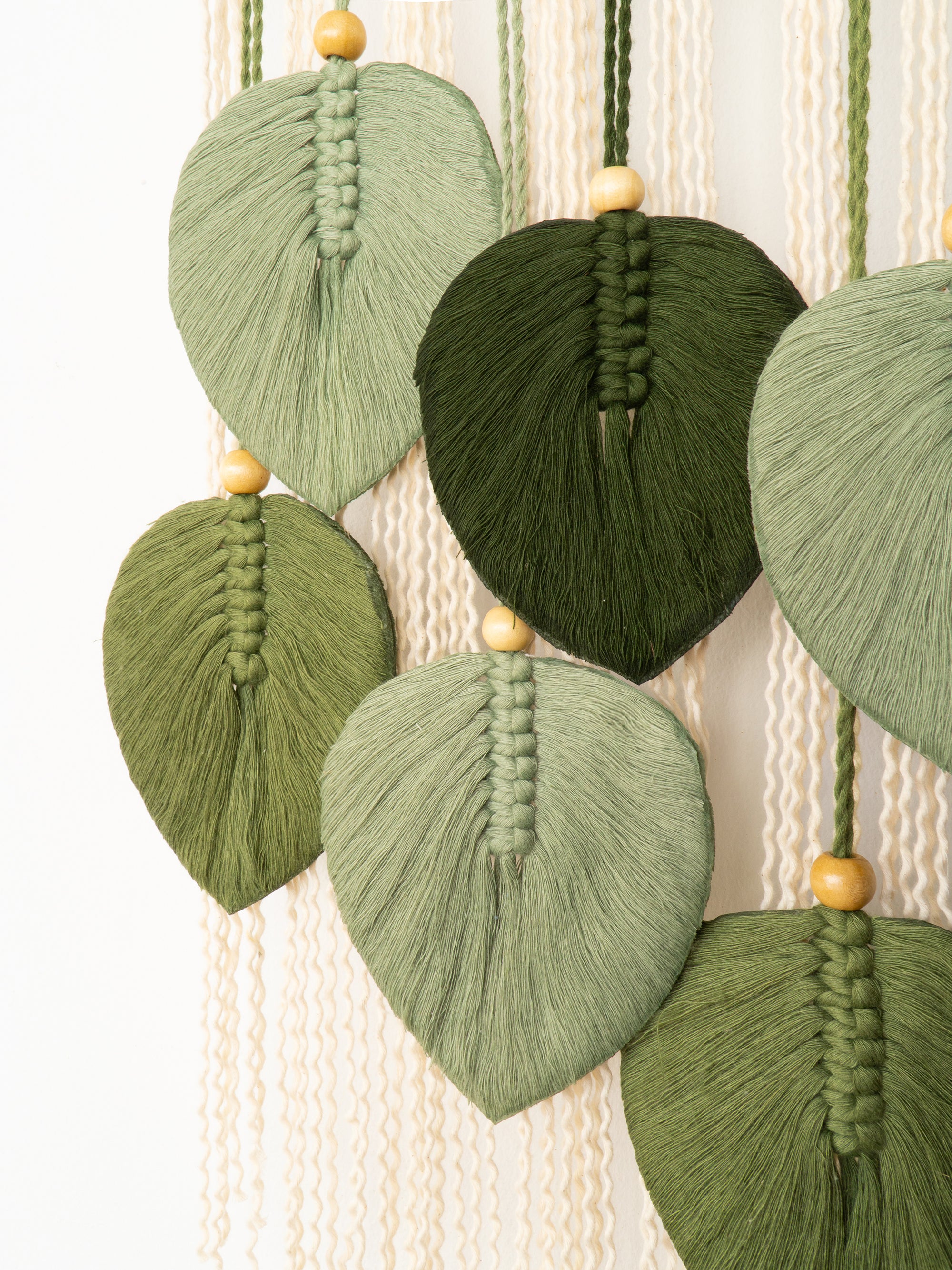 Green leaf-shaped macrame wall hanging with wooden beads on a white background
