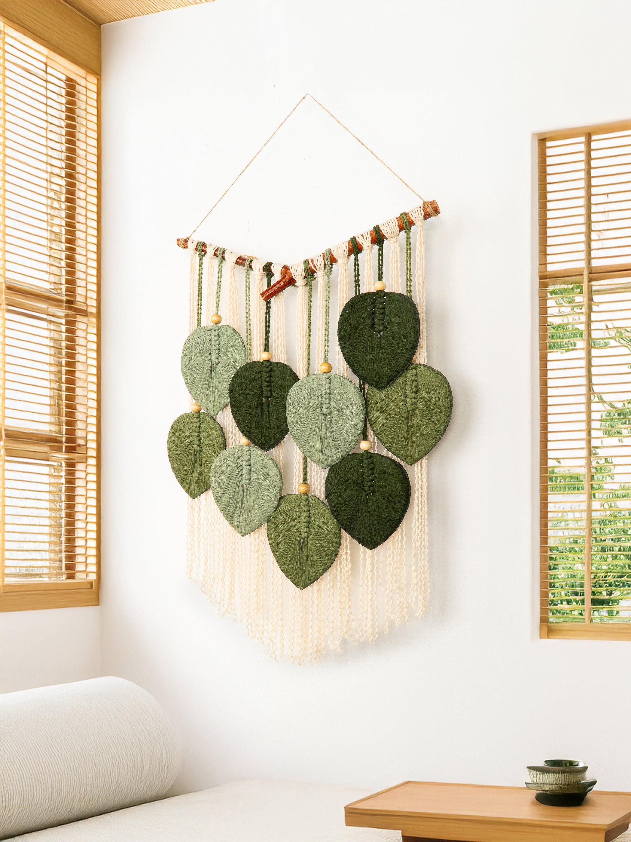 Decorative wall hanging with green leaf-shaped elements in a room with wooden blinds and a table.