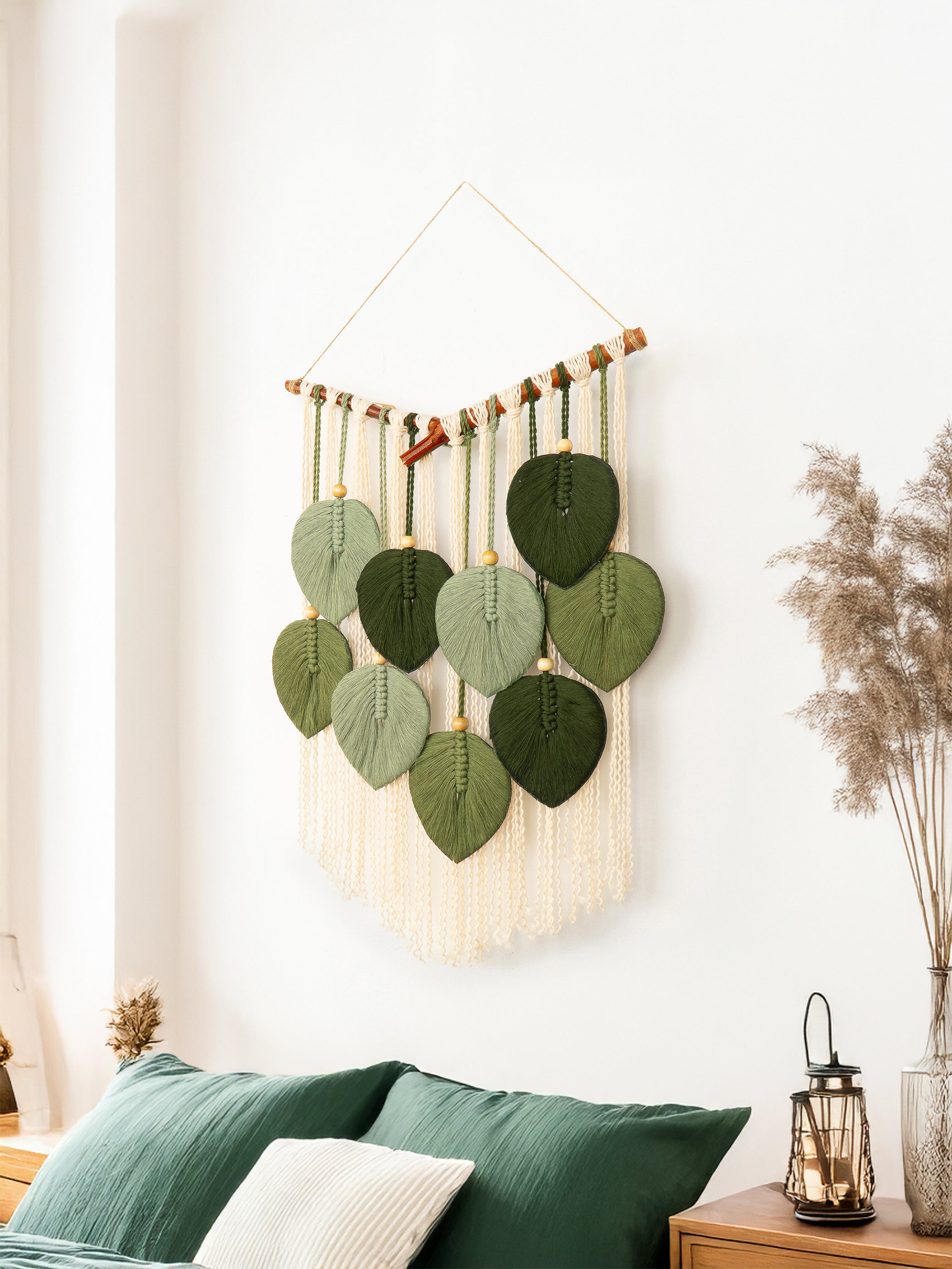 Decorative wall hanging with green leaf patterns and macrame details on a white wall.