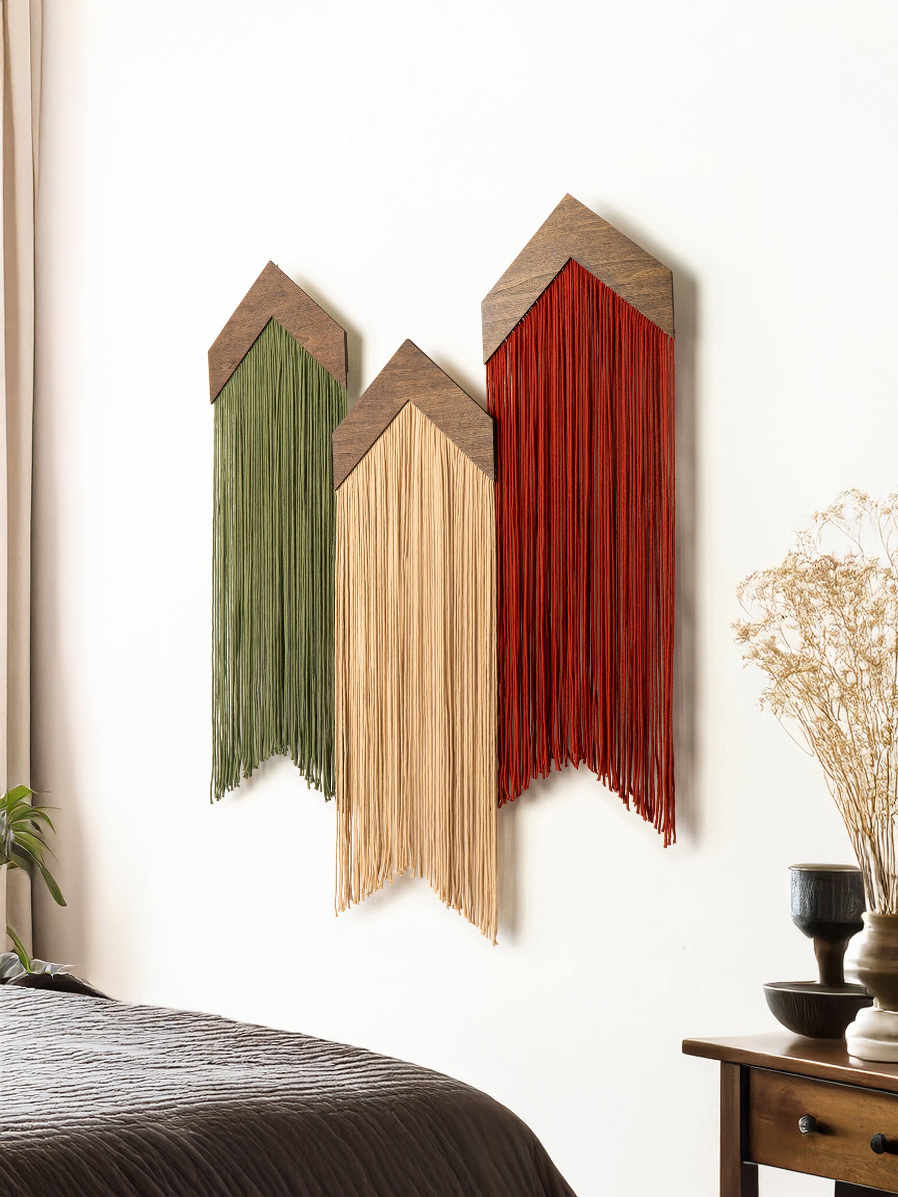 Three wooden wall art pieces with colorful fringe hanging on a white wall.
