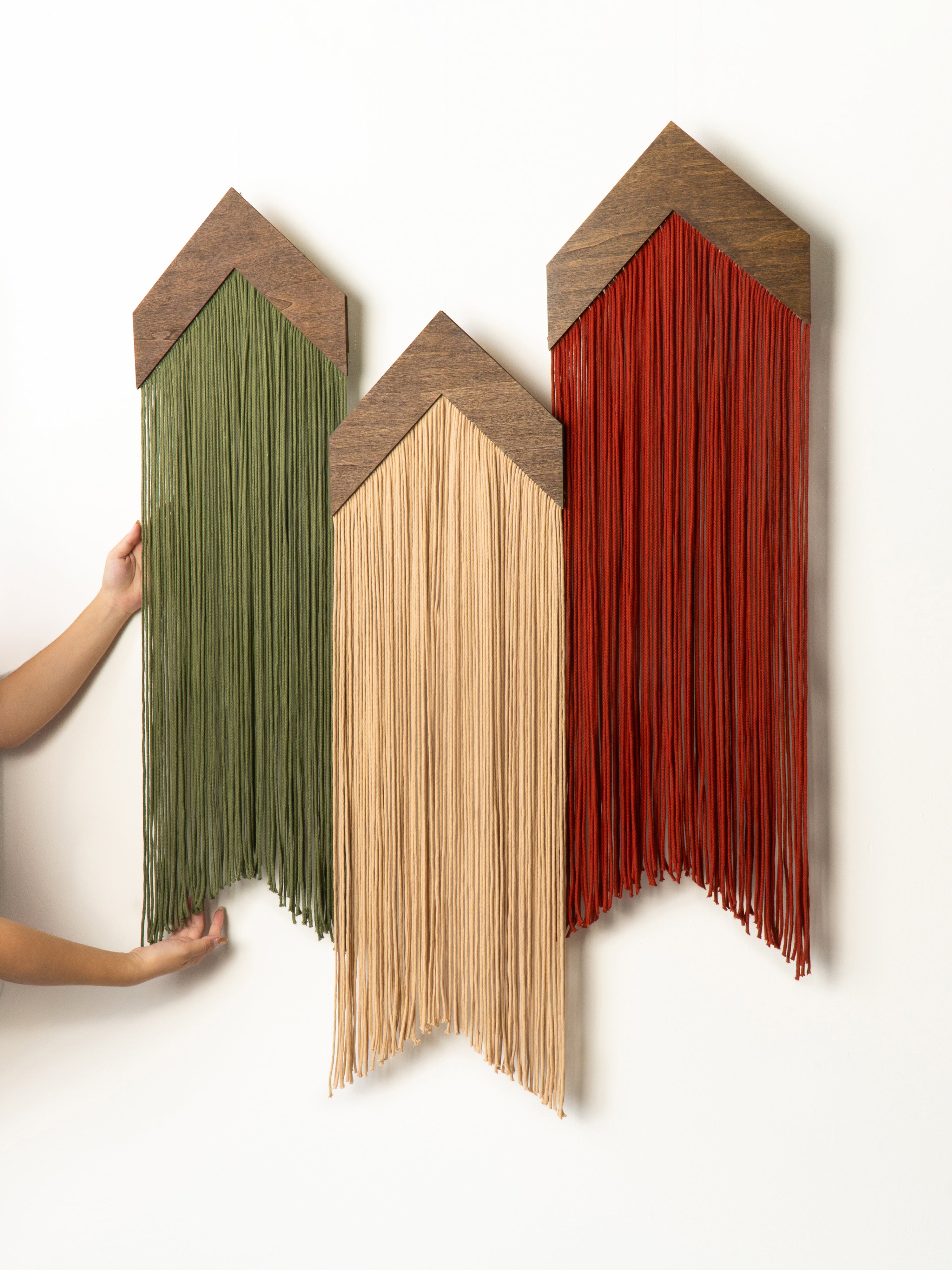 Three wooden wall art pieces with string hanging, each in a different color on a white background.