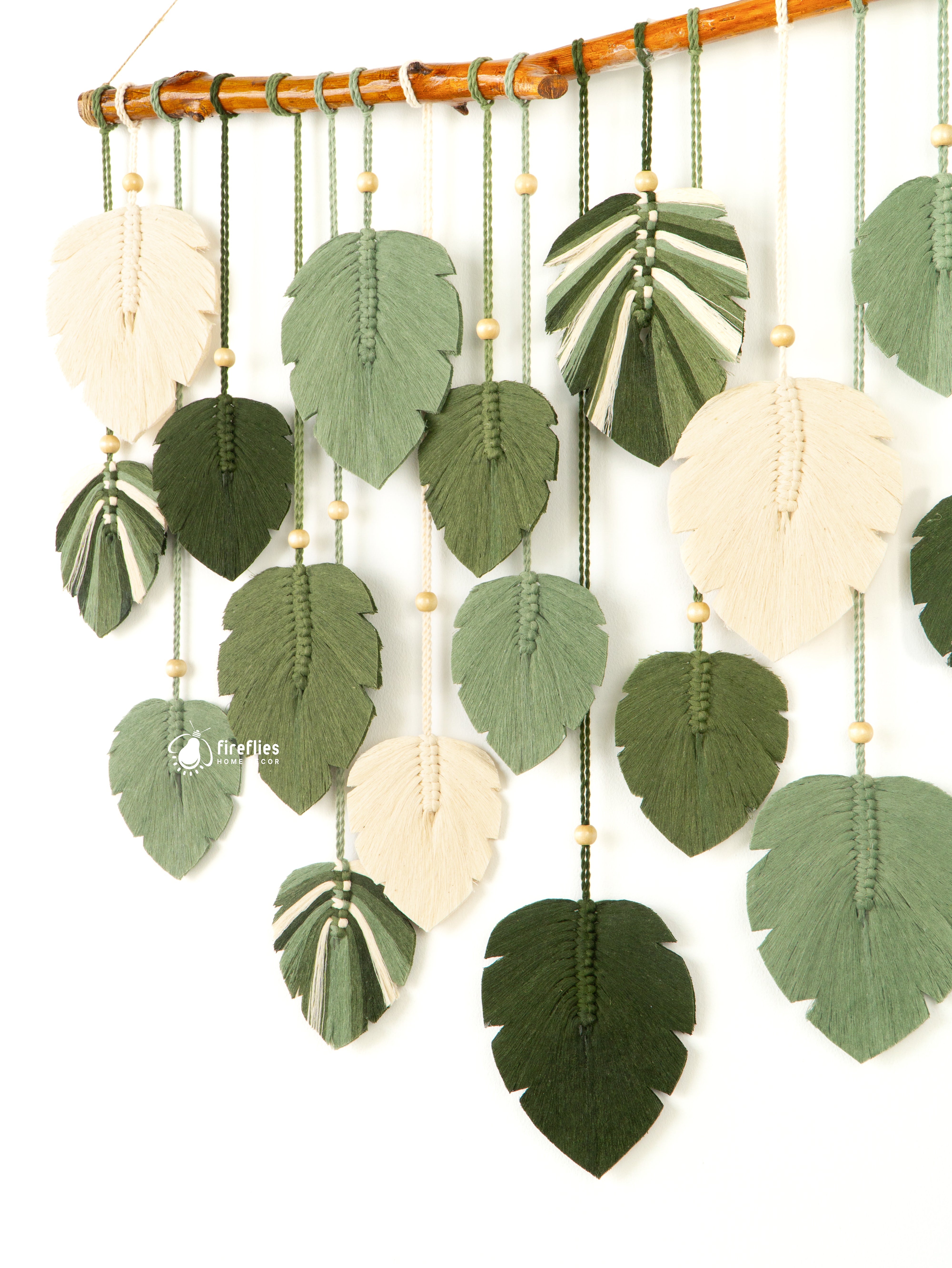 Decorative wall hanging with leaf-shaped green and beige elements on a white background
