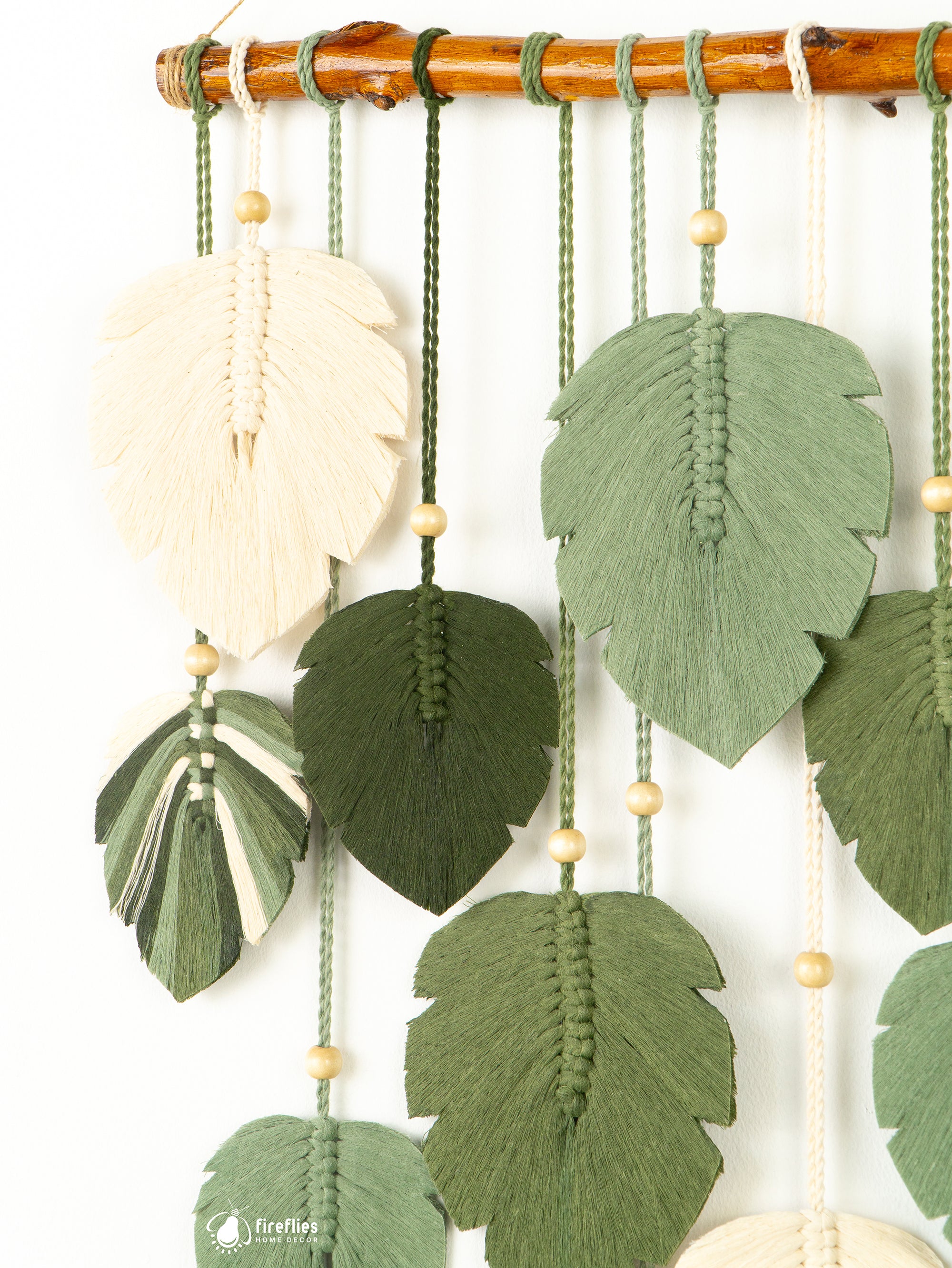 Decorative wall hanging with leaf-shaped fabric pieces and beads on a wooden rod.