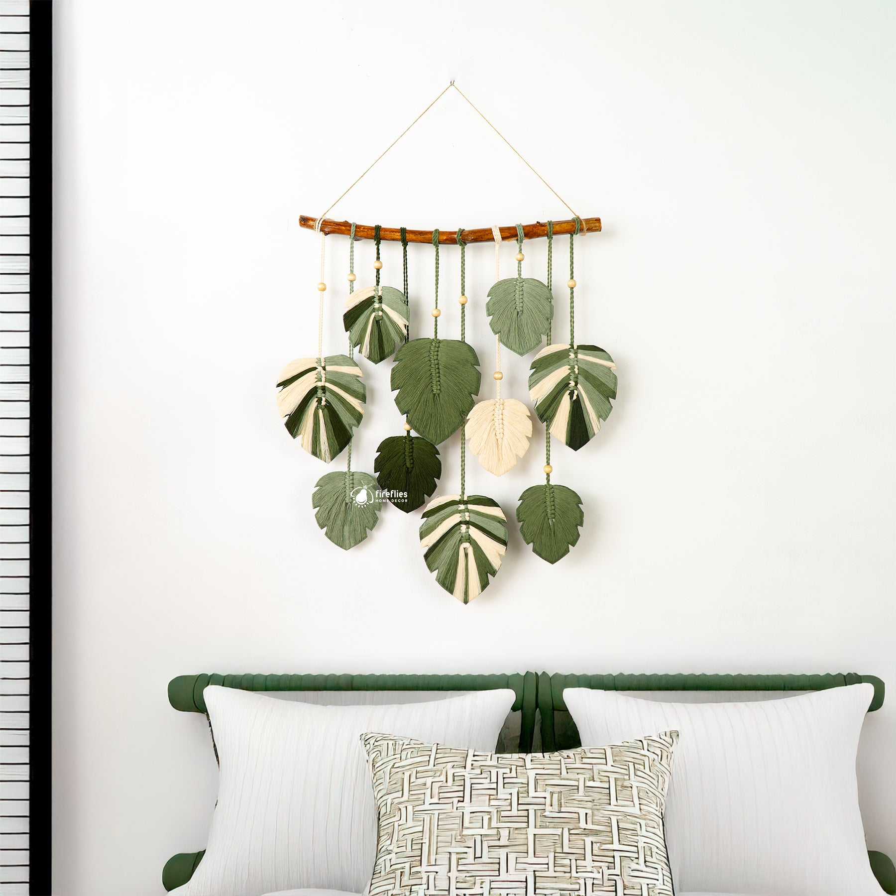 Decorative wall hanging with leaf patterns above a bed with white pillows and a green headboard.