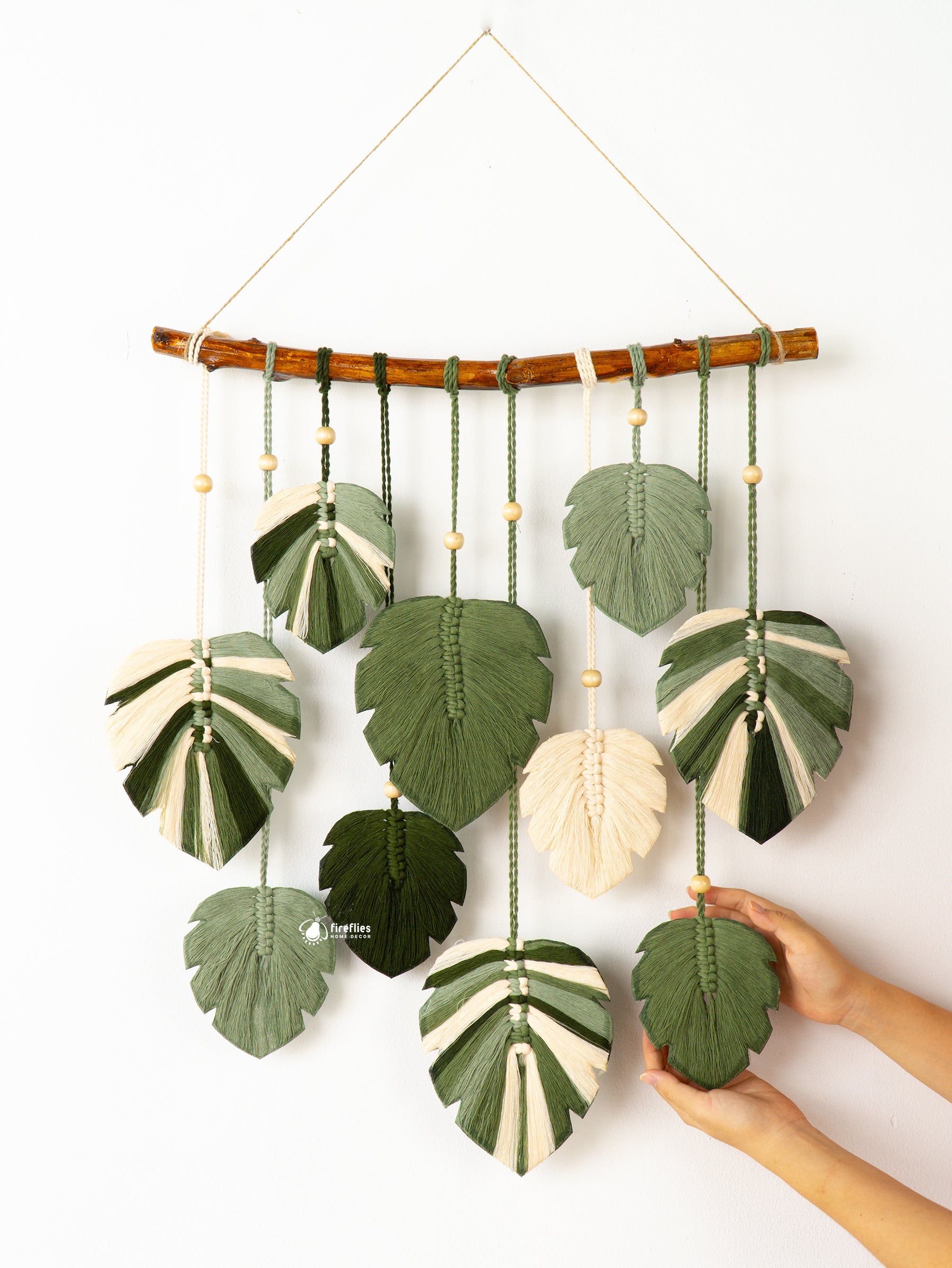 Decorative wall hanging with leaf-shaped green and beige elements on a white background