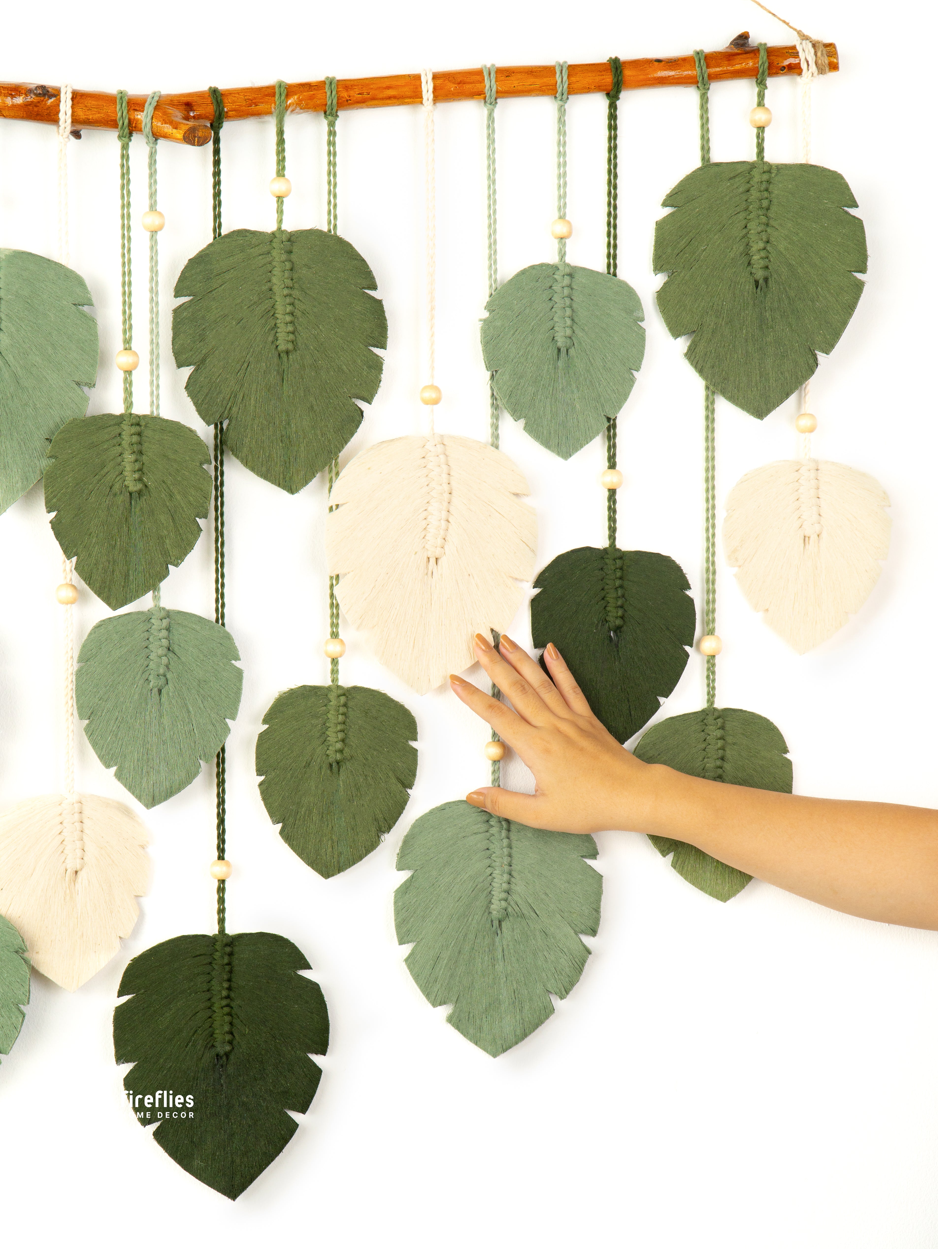 Decorative wall hanging with leaf-shaped panels and a hand touching one of them, on a white background.