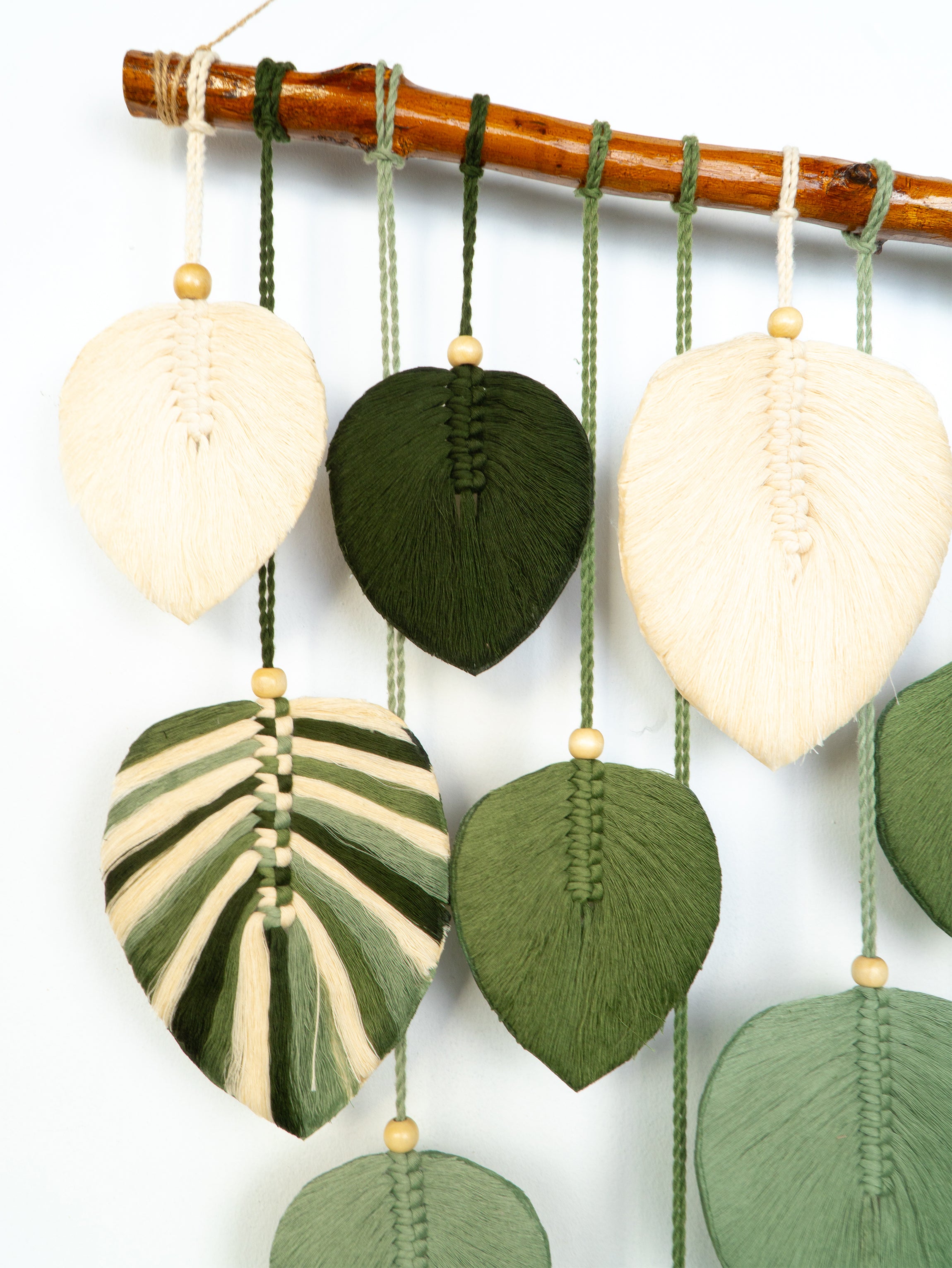 Decorative wall hanging with leaf-shaped green and beige elements on a white background