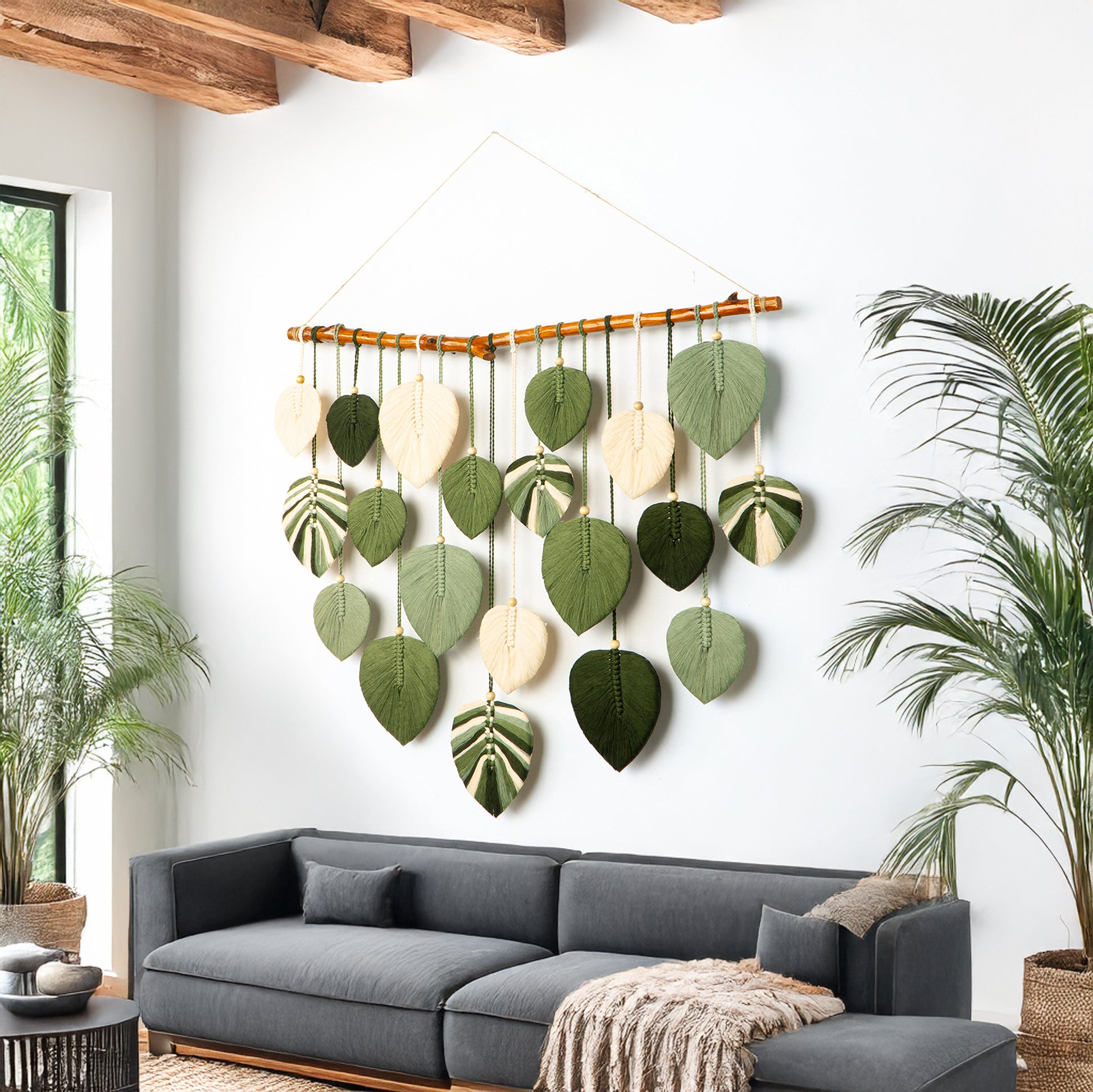 Decorative wall hanging with leaf patterns above a gray sofa in a room with plants.