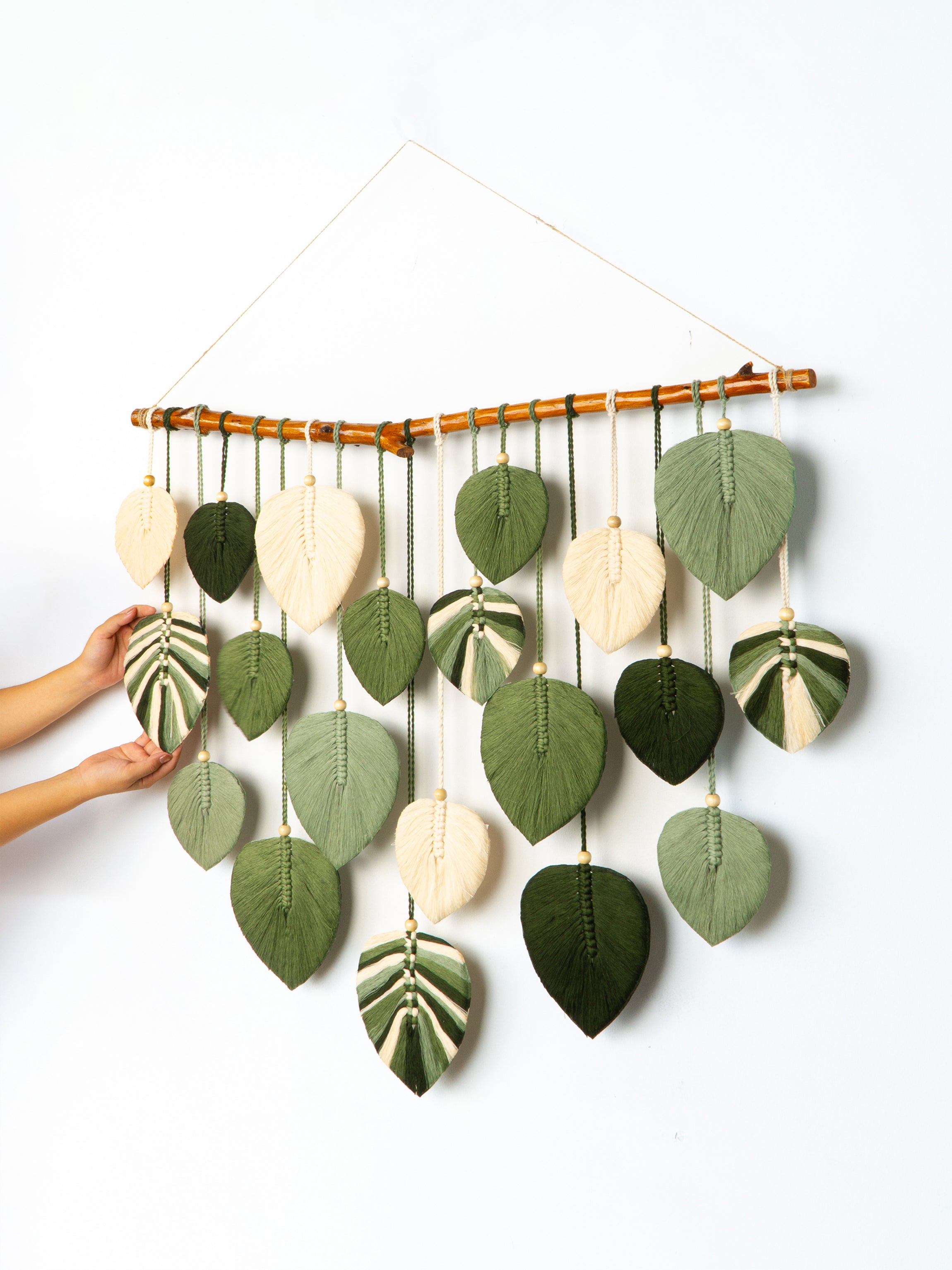 Decorative wall hanging with leaf-shaped green and beige elements on a white background