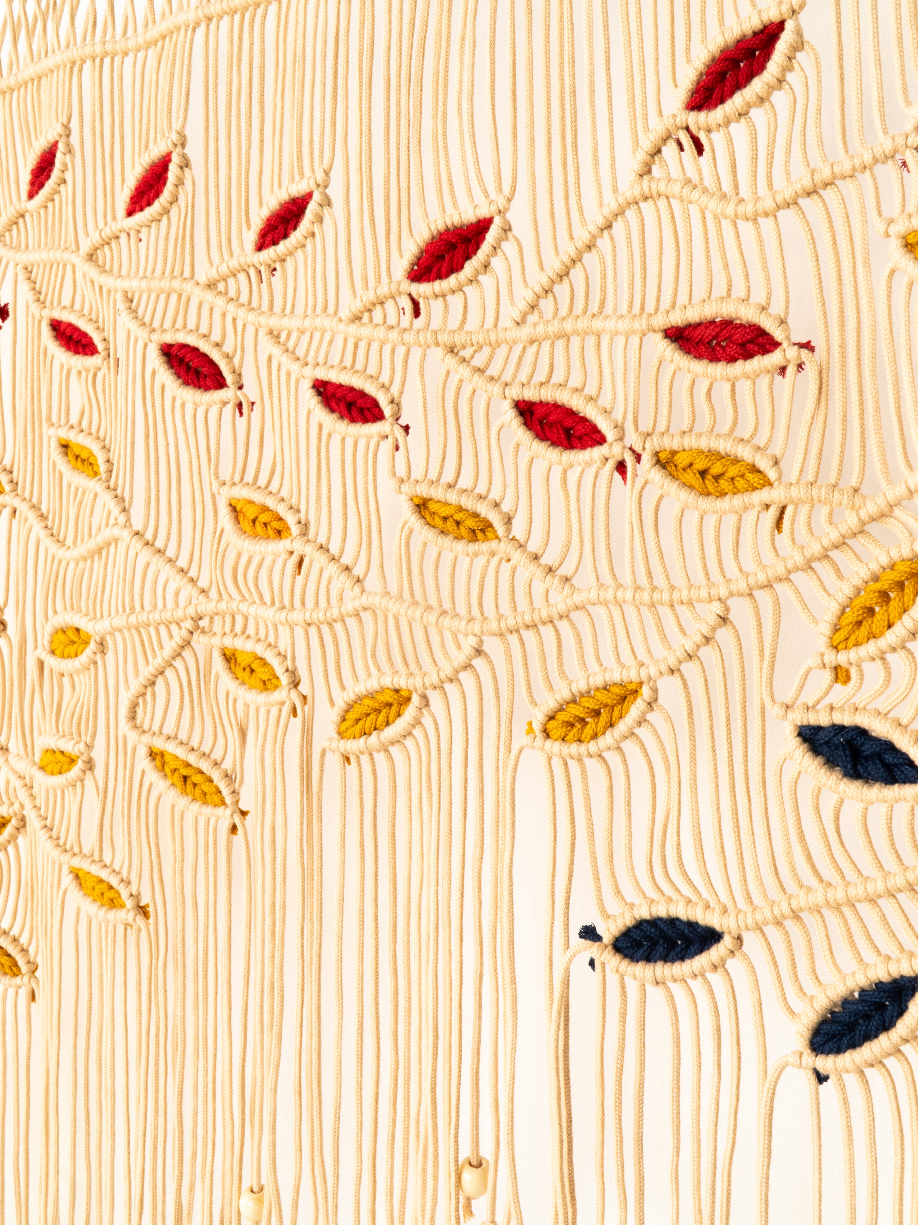 Close-up of a textured fabric with embroidered leaves in red, yellow, and black on a beige background.