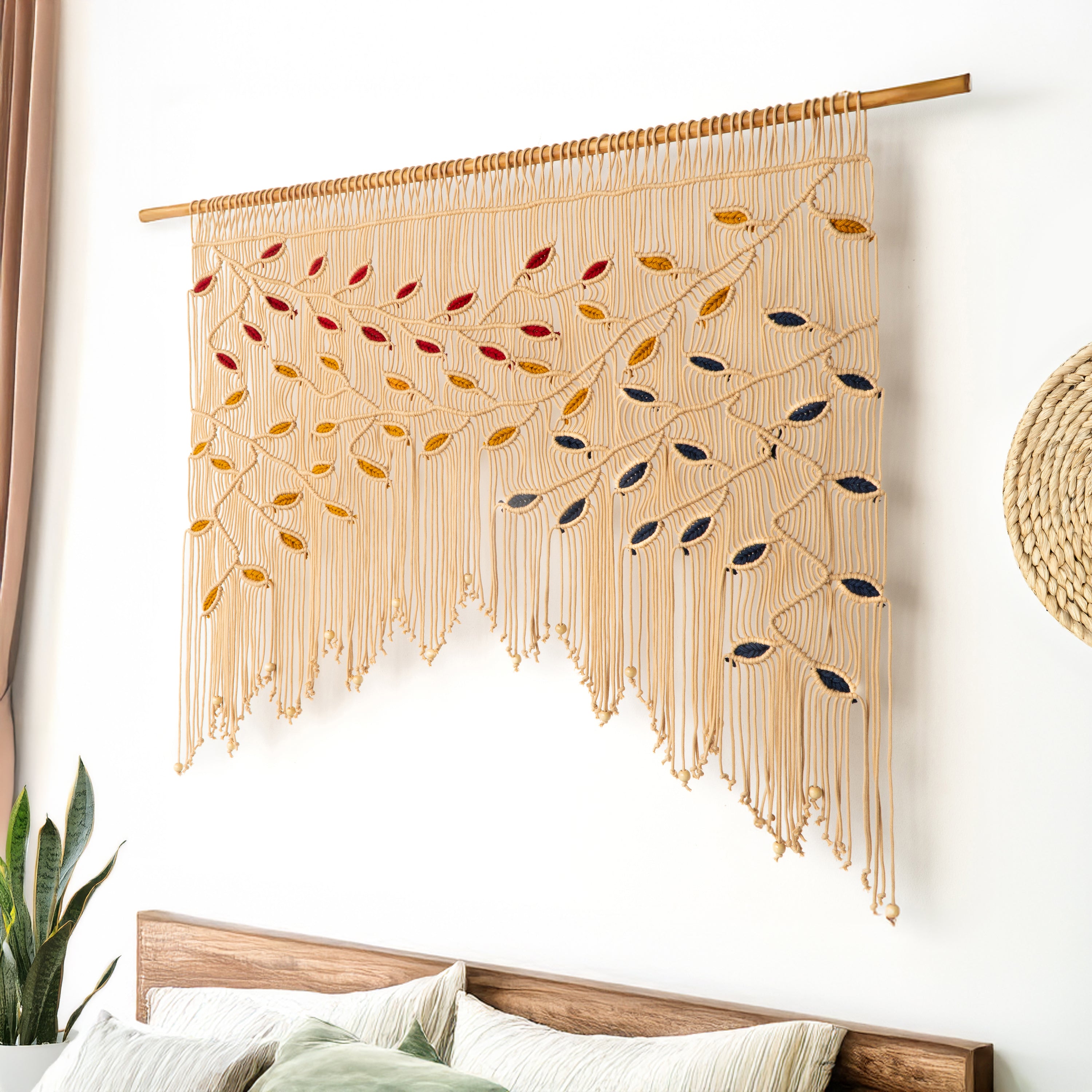 Macrame wall hanging with leaf patterns on a white wall above a bed.