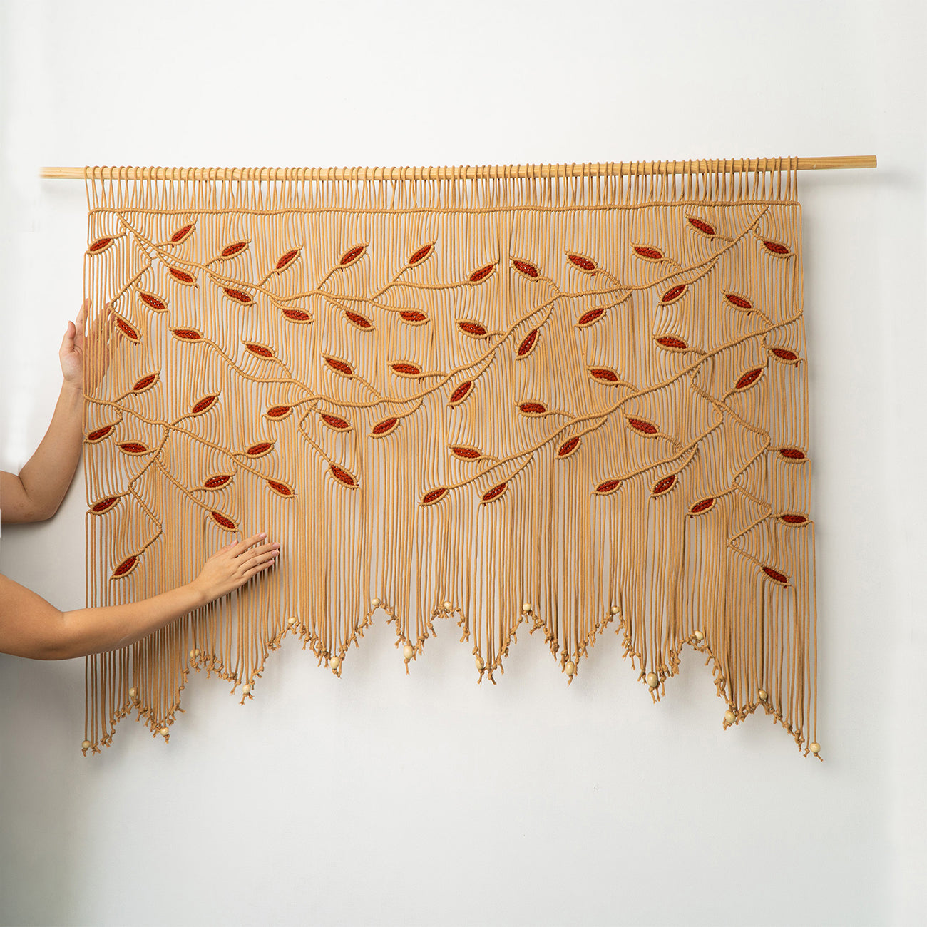 Intricate beige fiber art headboard with cascading terracotta leaf vines and a beaded scalloped edge.