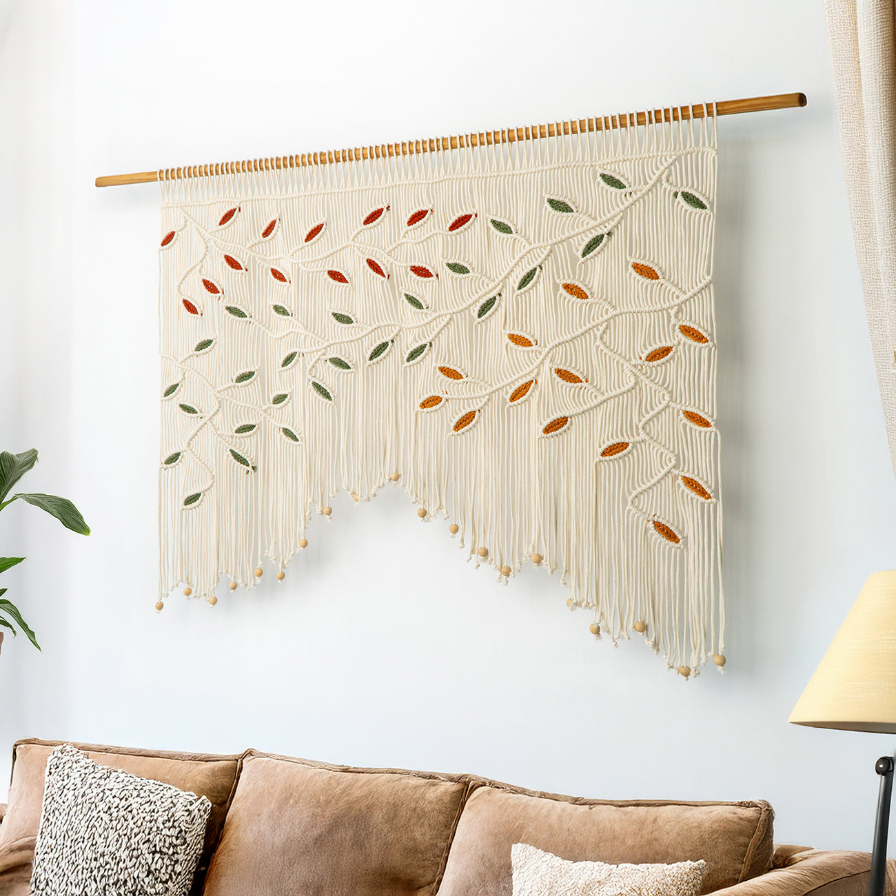 Wide horizontal fiber art in cream macrame cord featuring a multi-color botanical vine design.