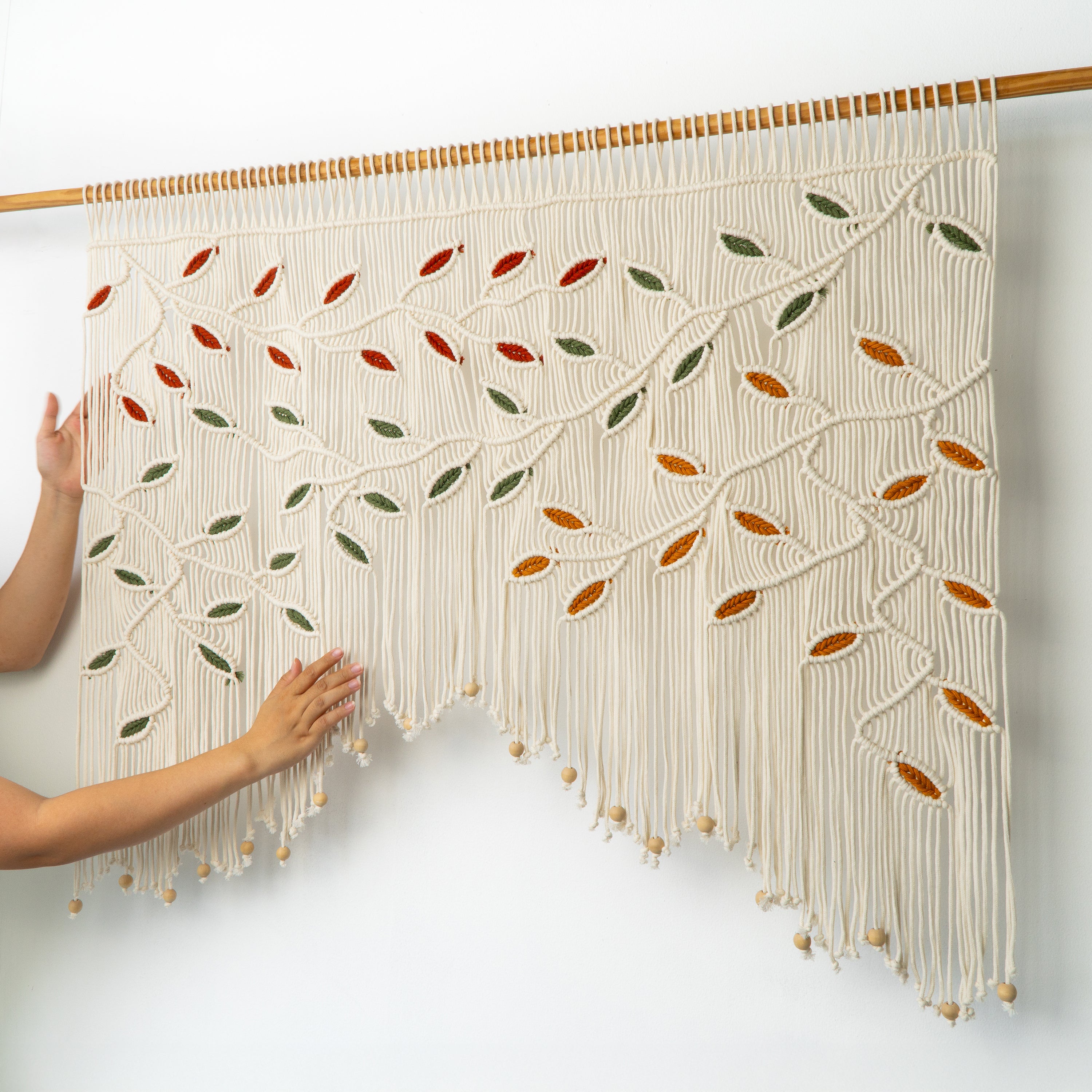 Macrame wall hanging with leaf patterns held by a person against a white background