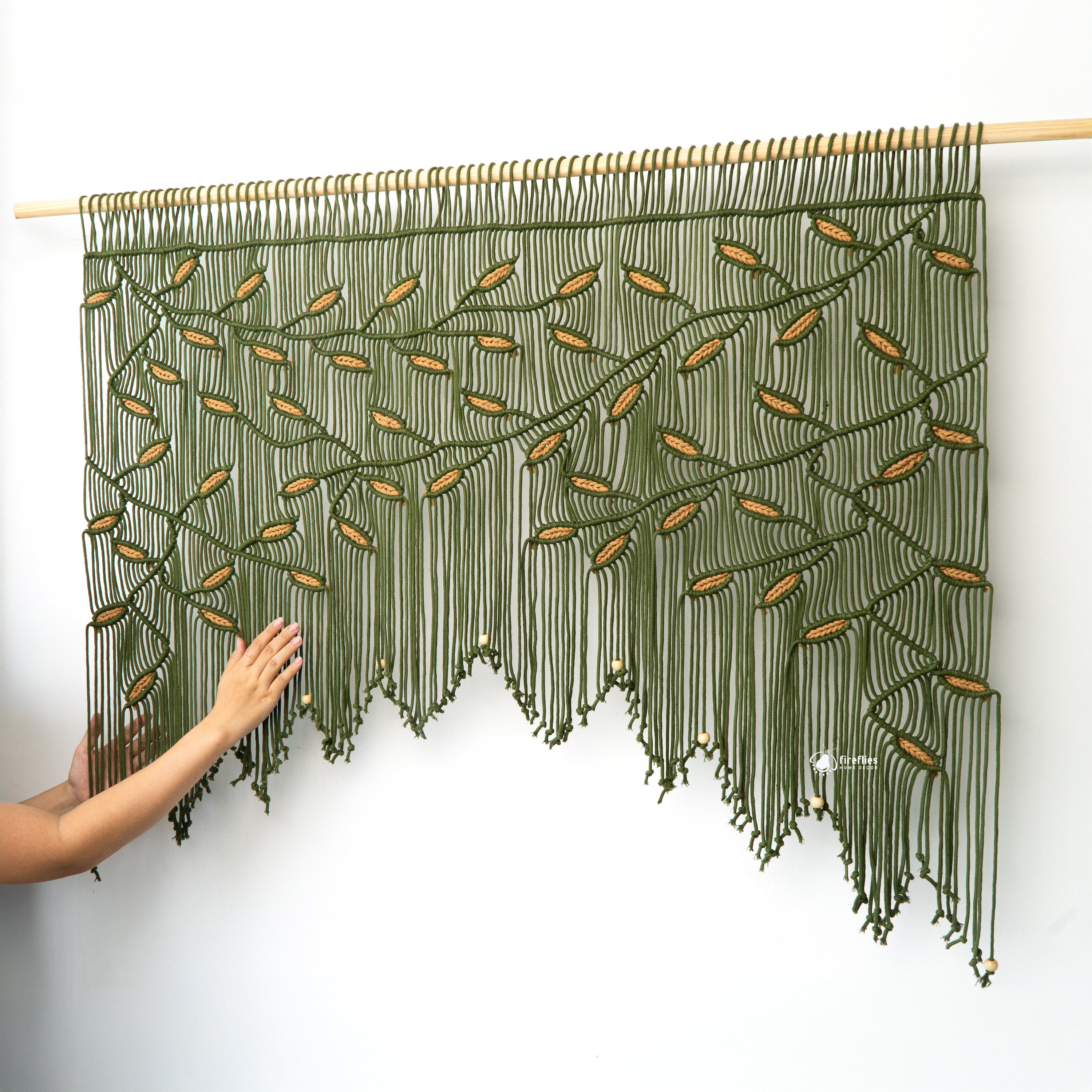 Handmade wall hanging with green and gold threads on a white background