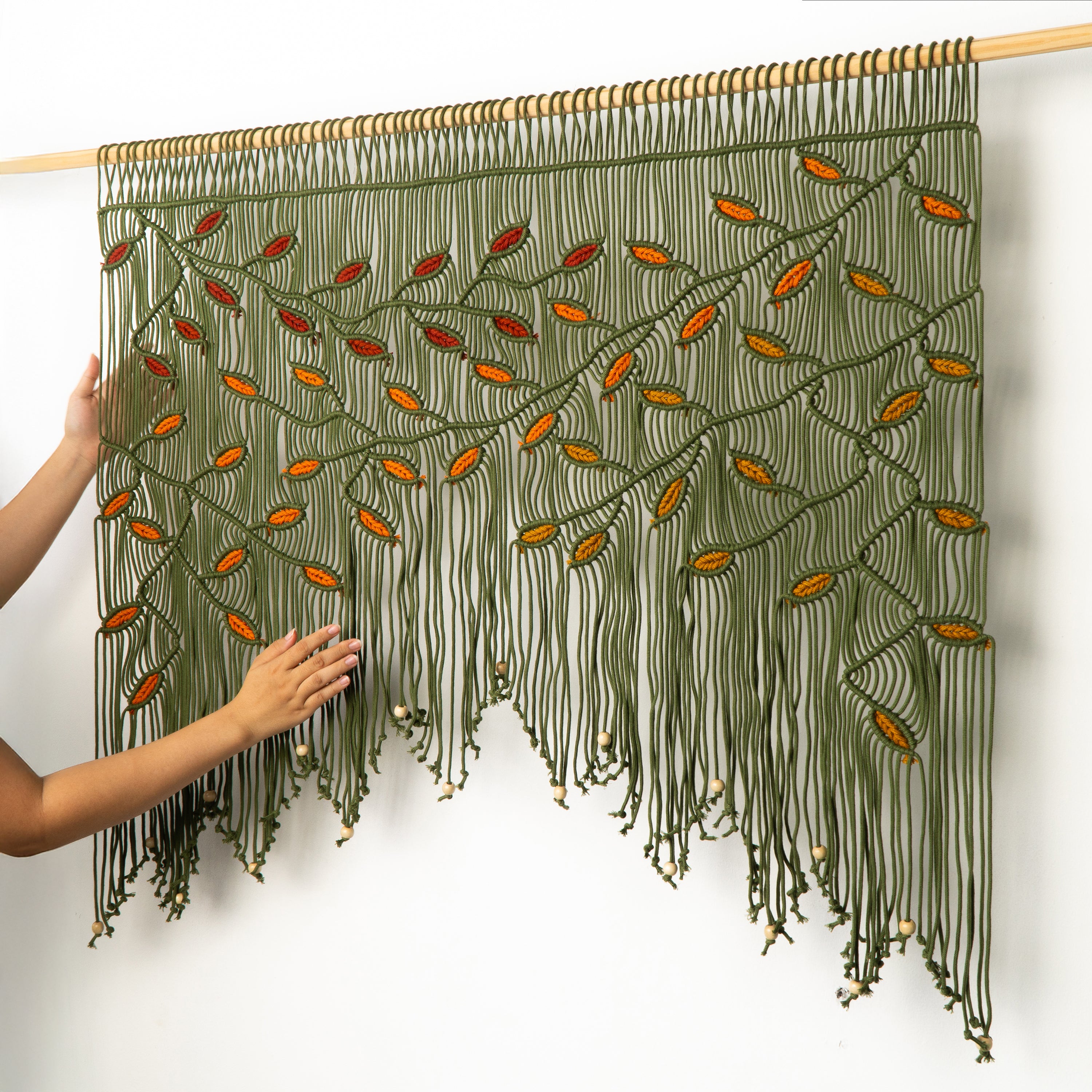 Handmade macrame wall hanging with green and orange pattern on a white background