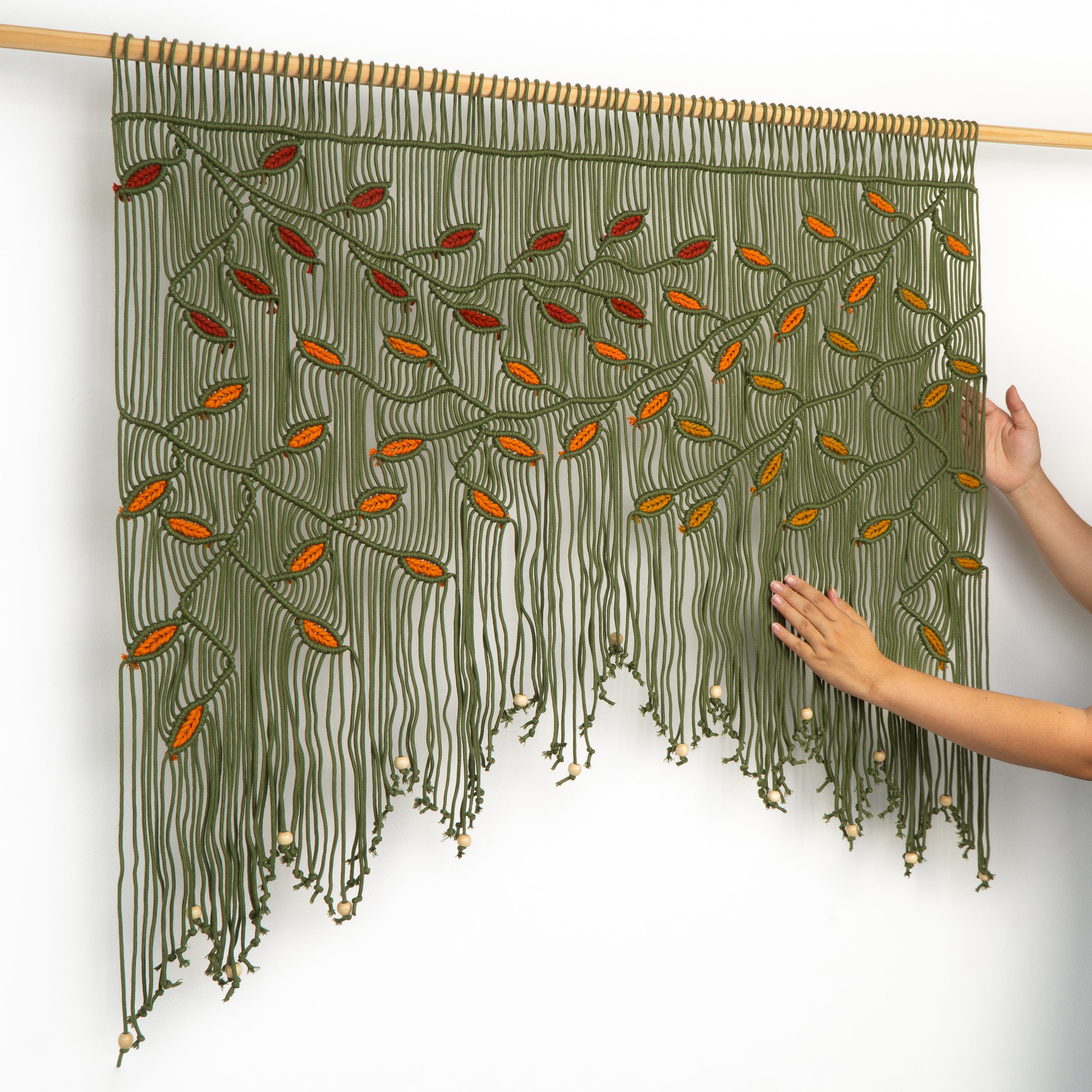 Textile art piece with green and orange pattern held by hands on a white background