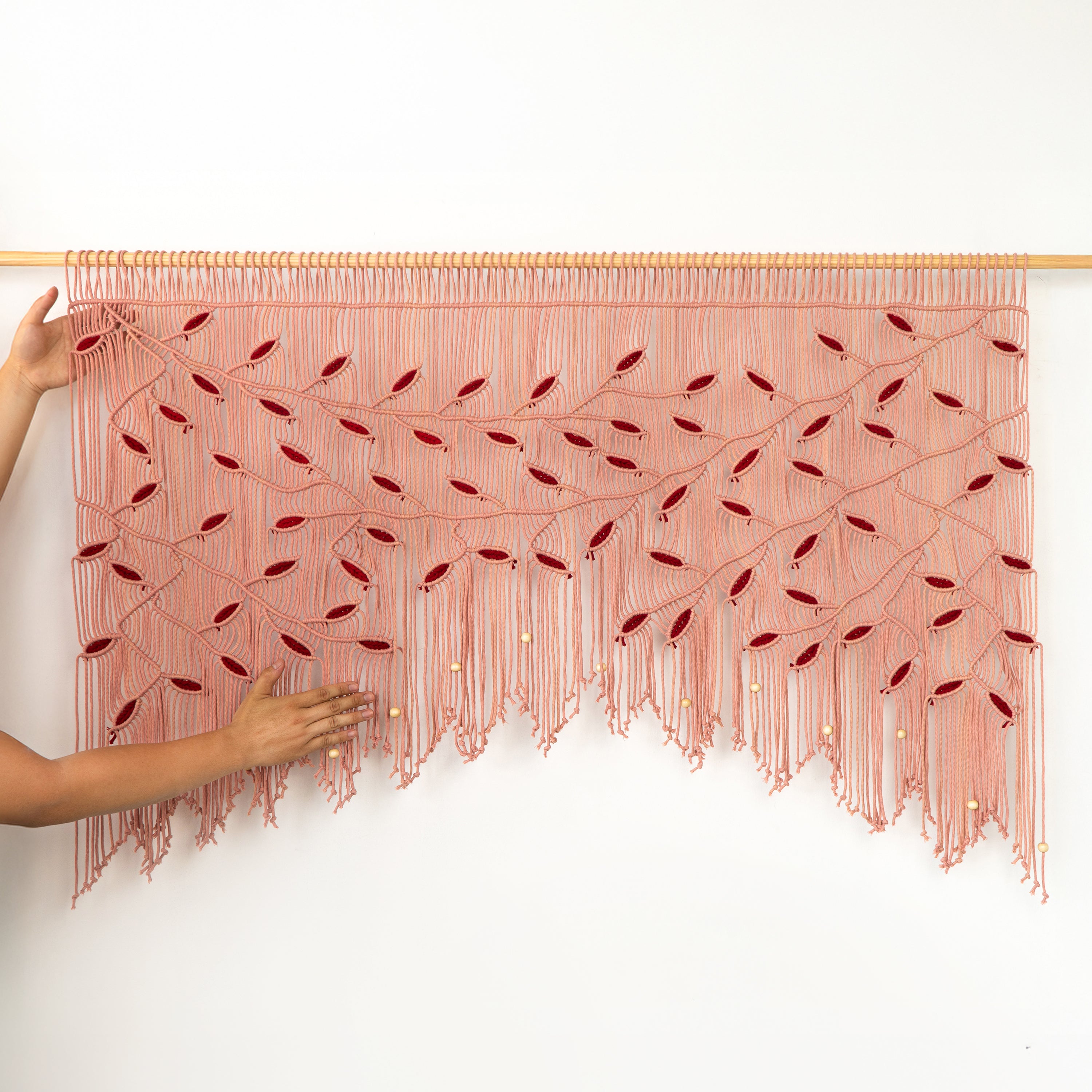 Pink woven wall art with red accents held by a person against a white background