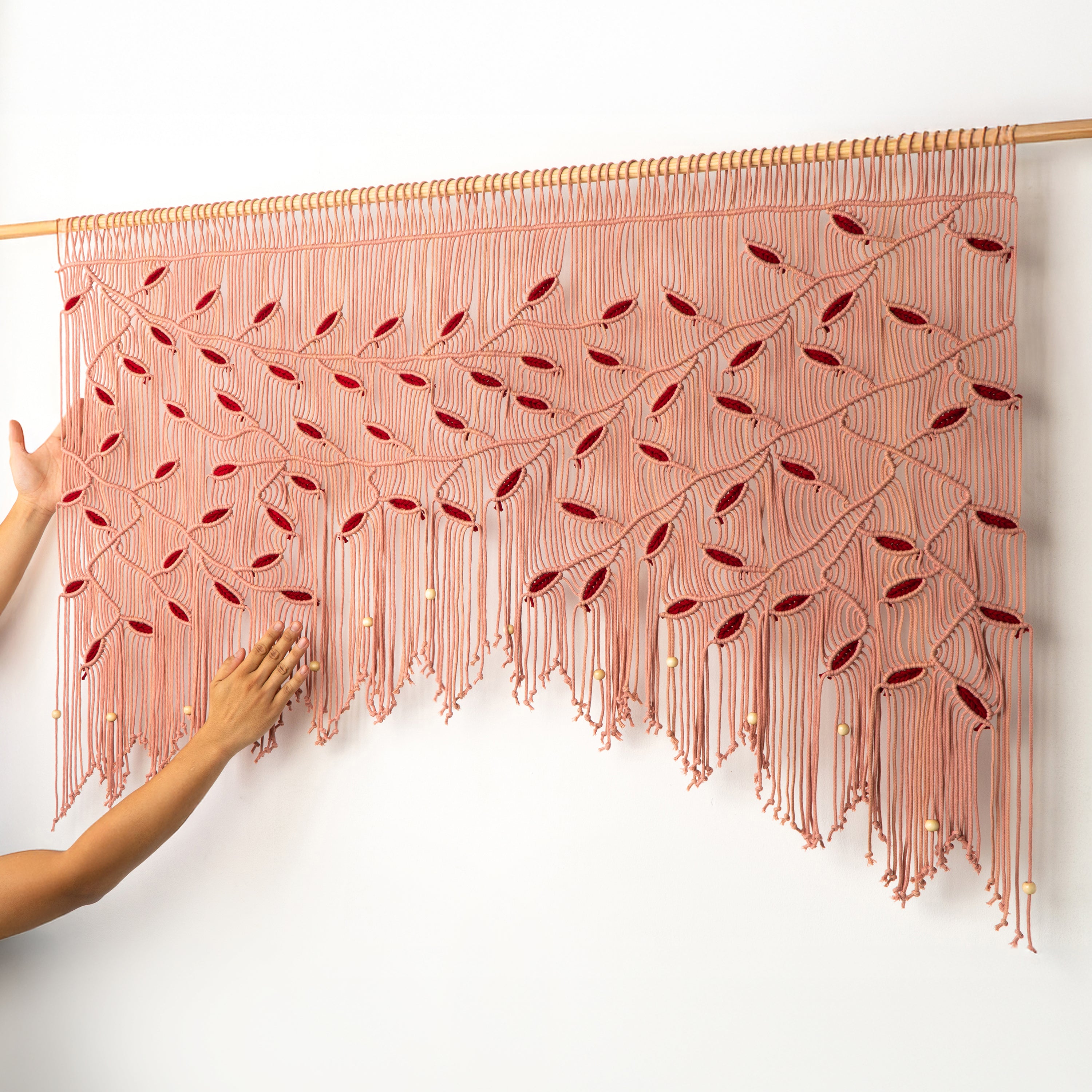 Pink macramé wall hanging with red accents on a white background