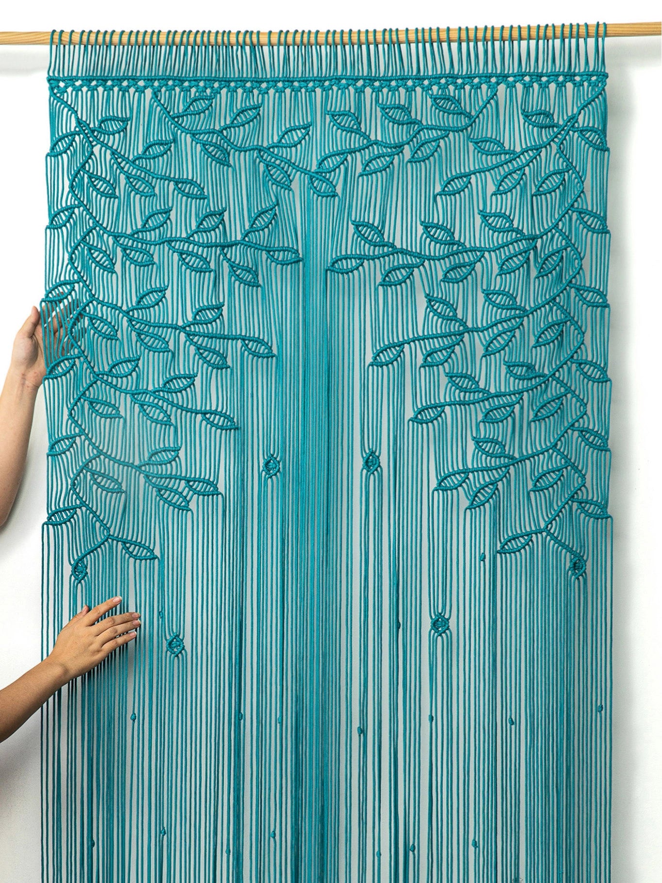 Handcrafted bohemian doorway divider featuring knotted aqua blue leafy branches and draped fringe cords.