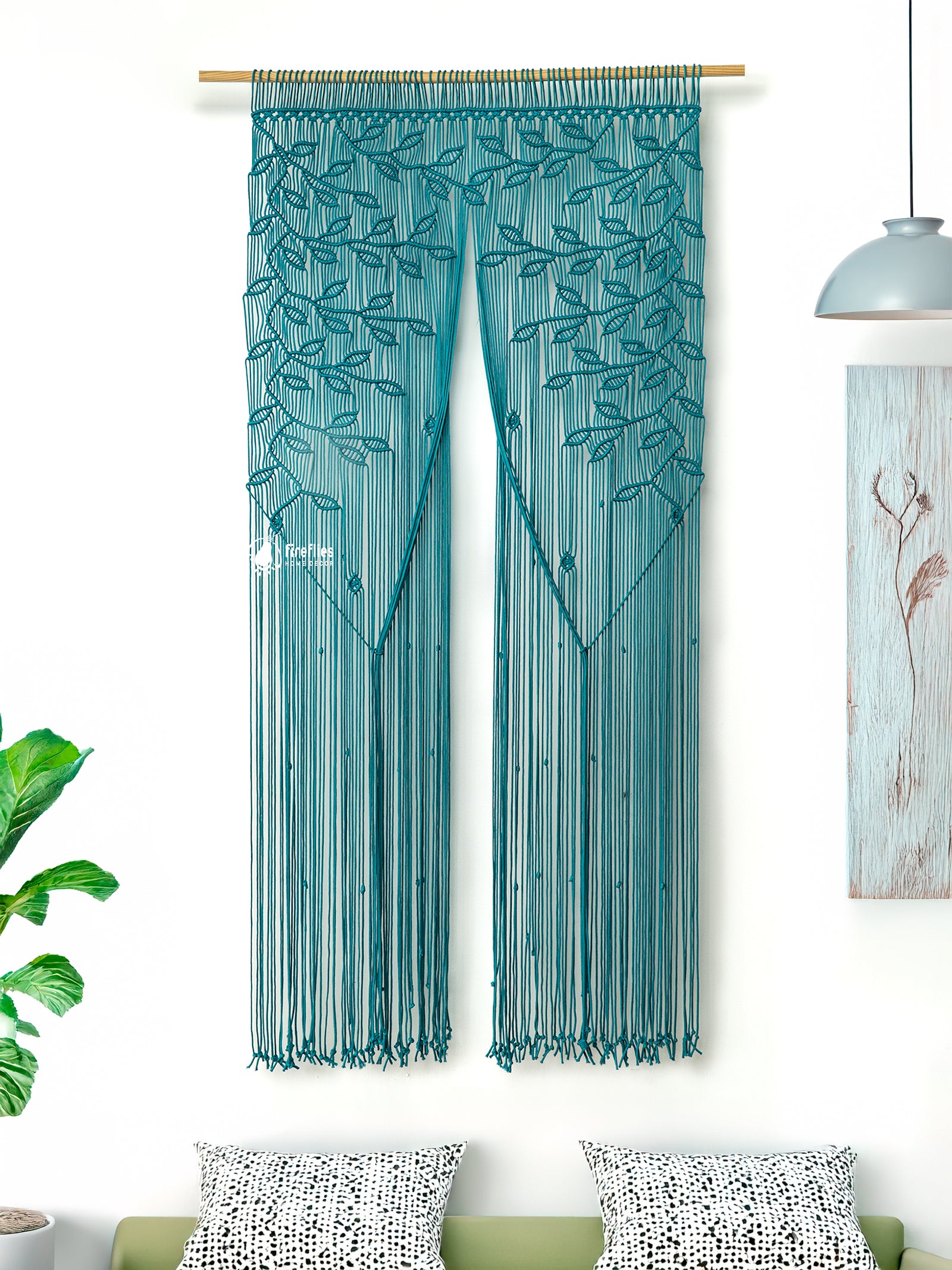 Teal string curtain with leaf pattern on a white wall with decorative pillows and plant.