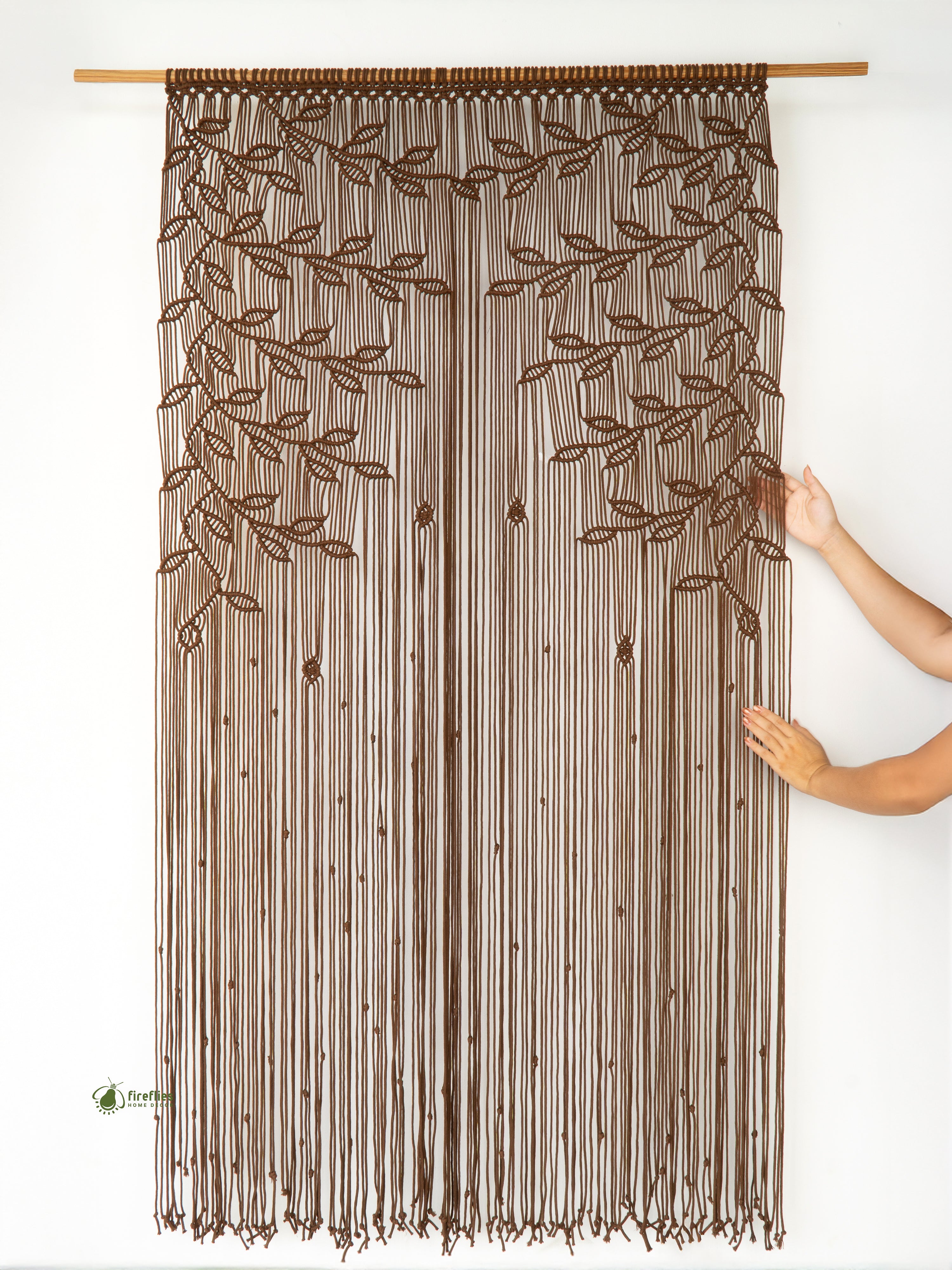 Brown beaded curtain with leaf pattern held by a hand against a white background