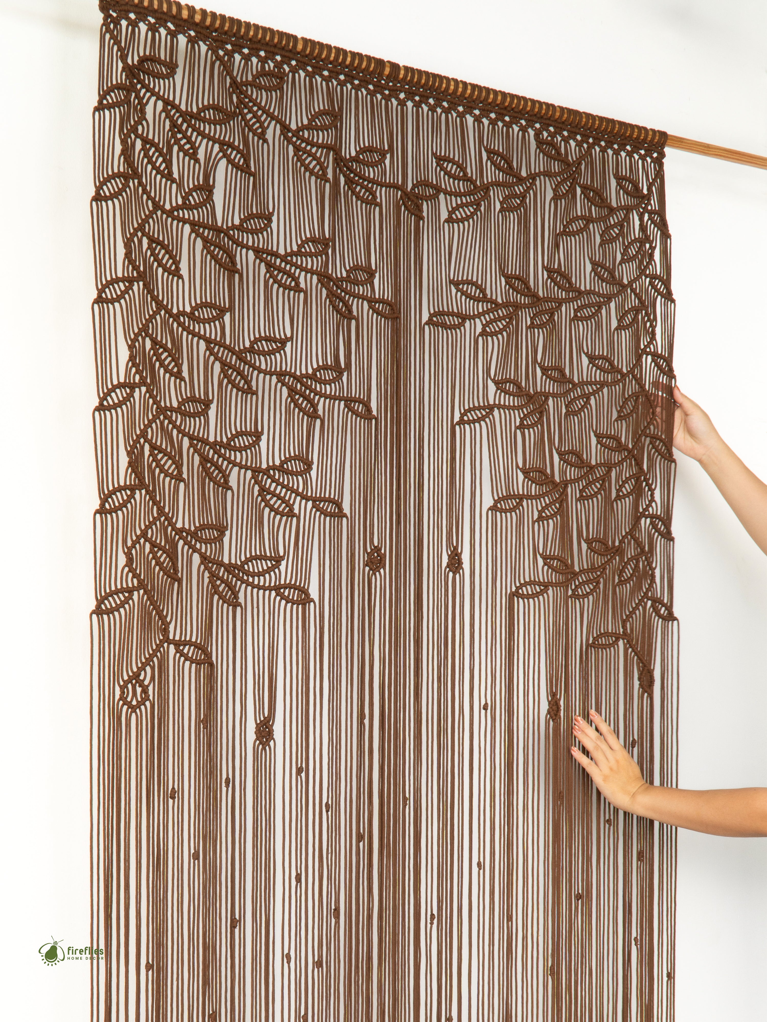 Brown beaded curtain with leaf patterns held by a person against a white background