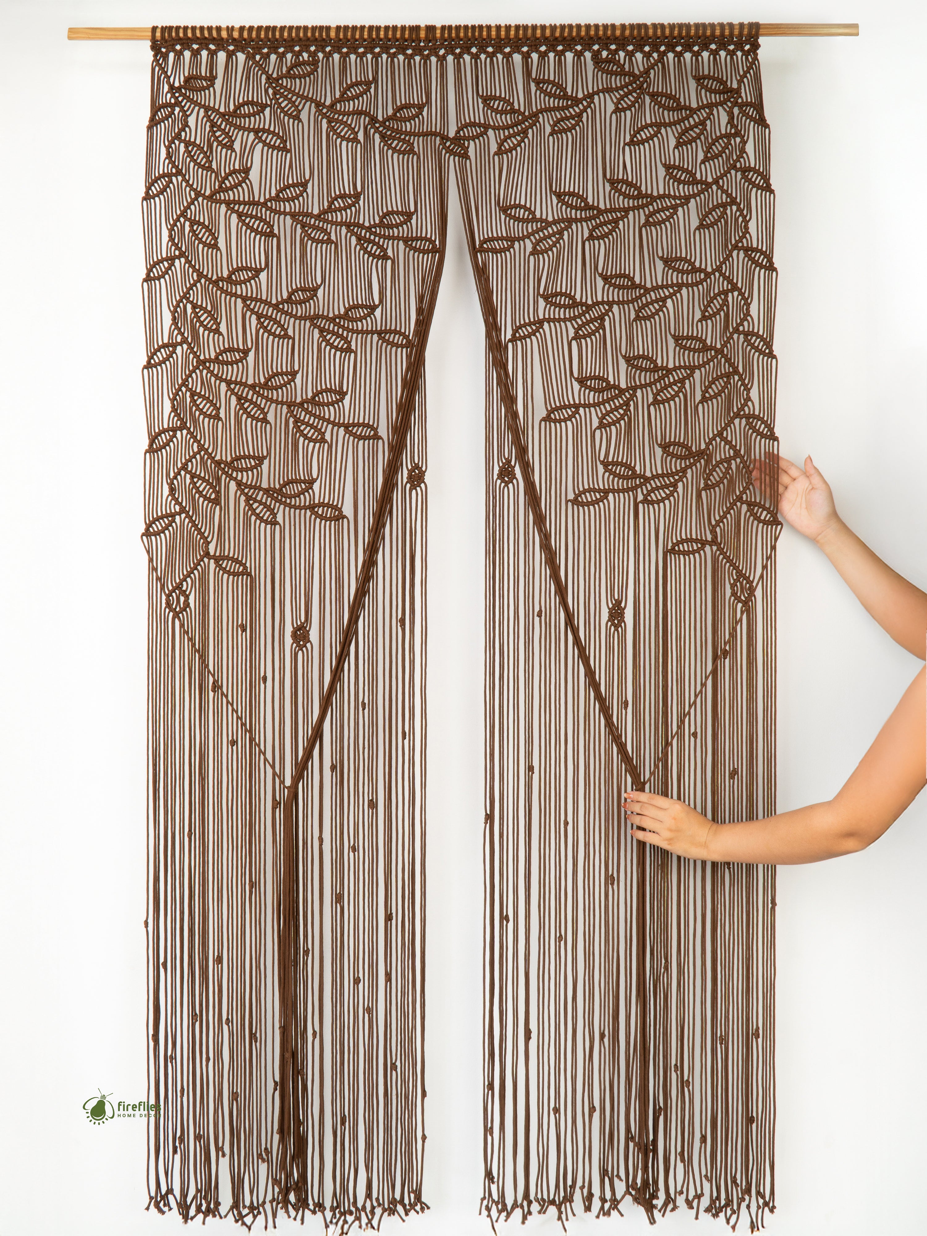 Brown beaded curtain with leaf pattern held by a hand against a white background