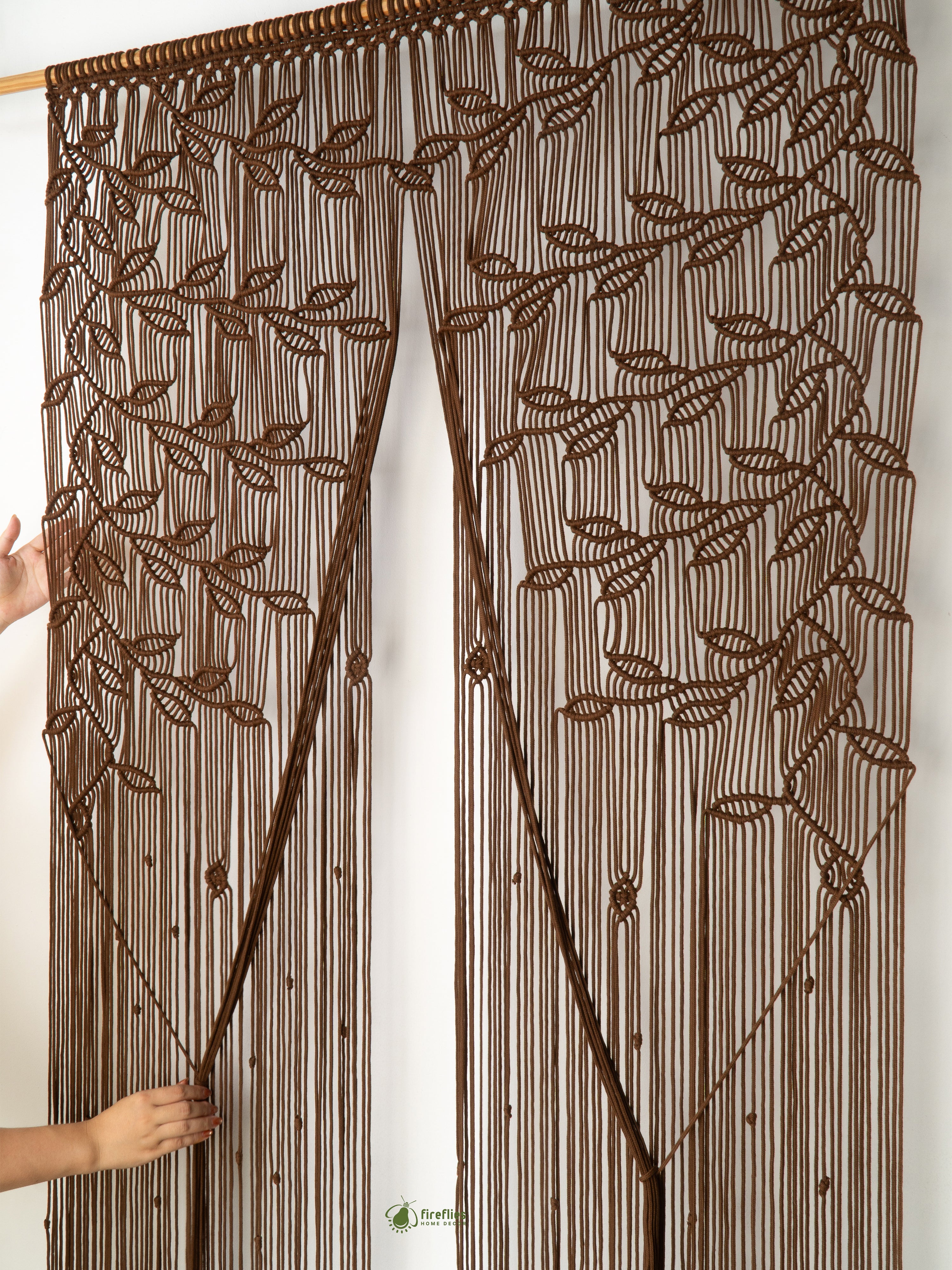 Brown beaded curtain with leaf pattern held by a person against a white background