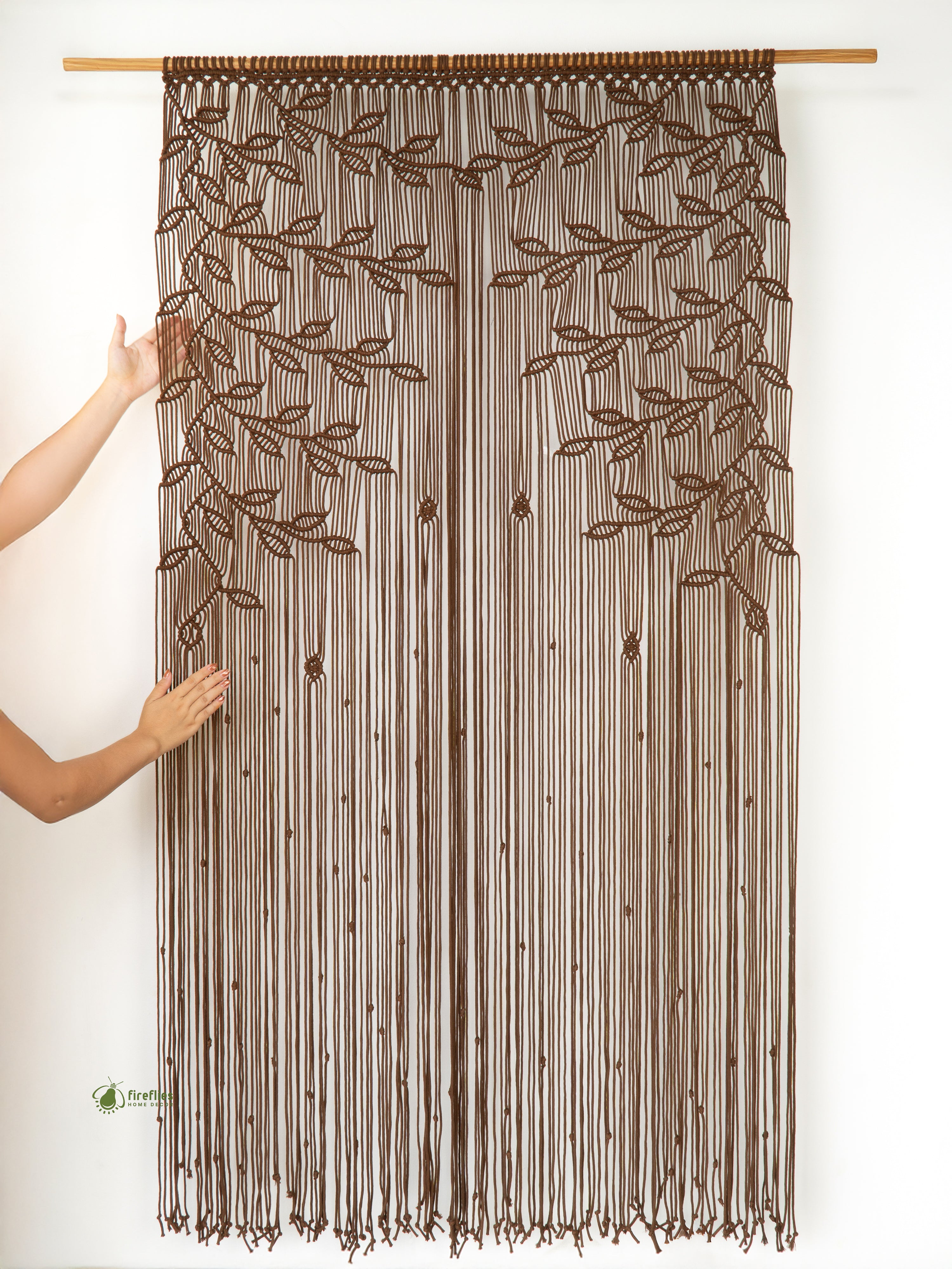 Brown beaded curtain with leaf patterns held up by a person against a white background