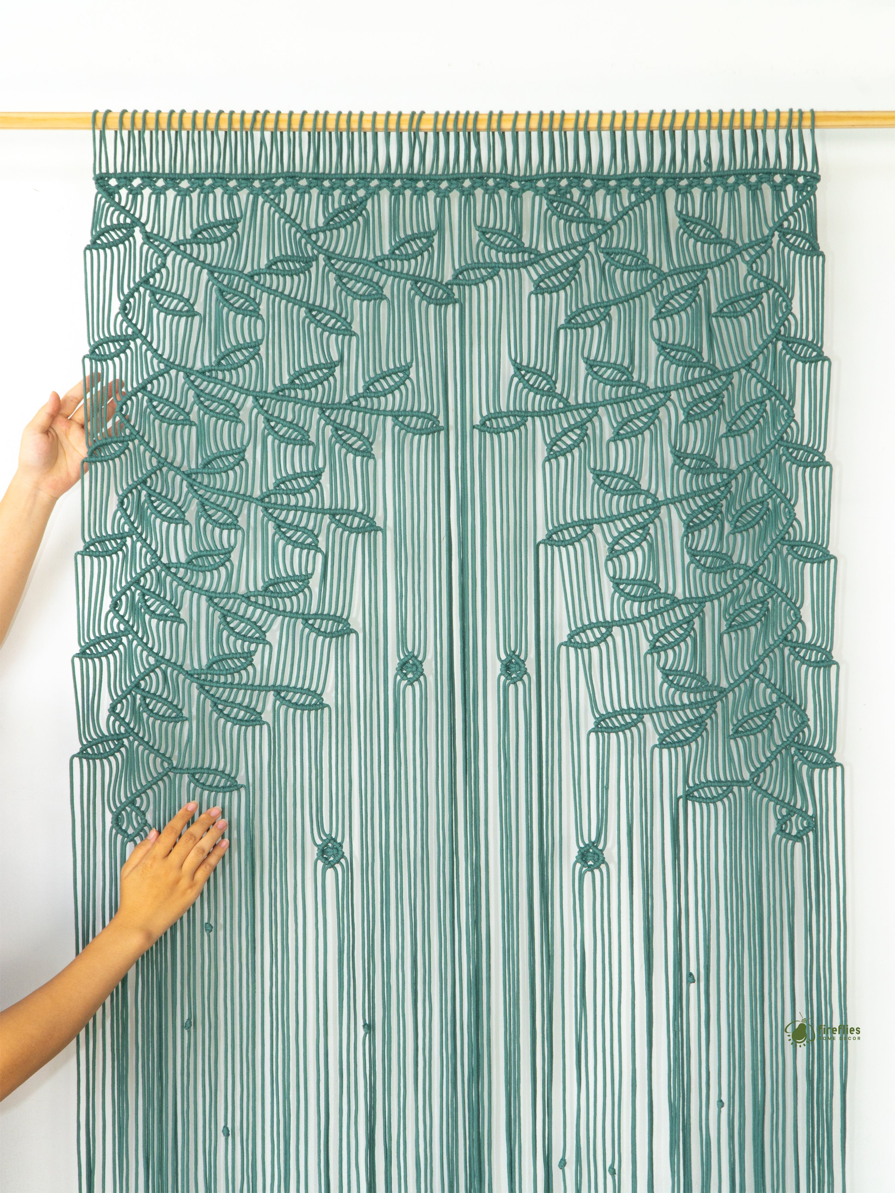 Green string curtain with leaf pattern held by a person against a white background