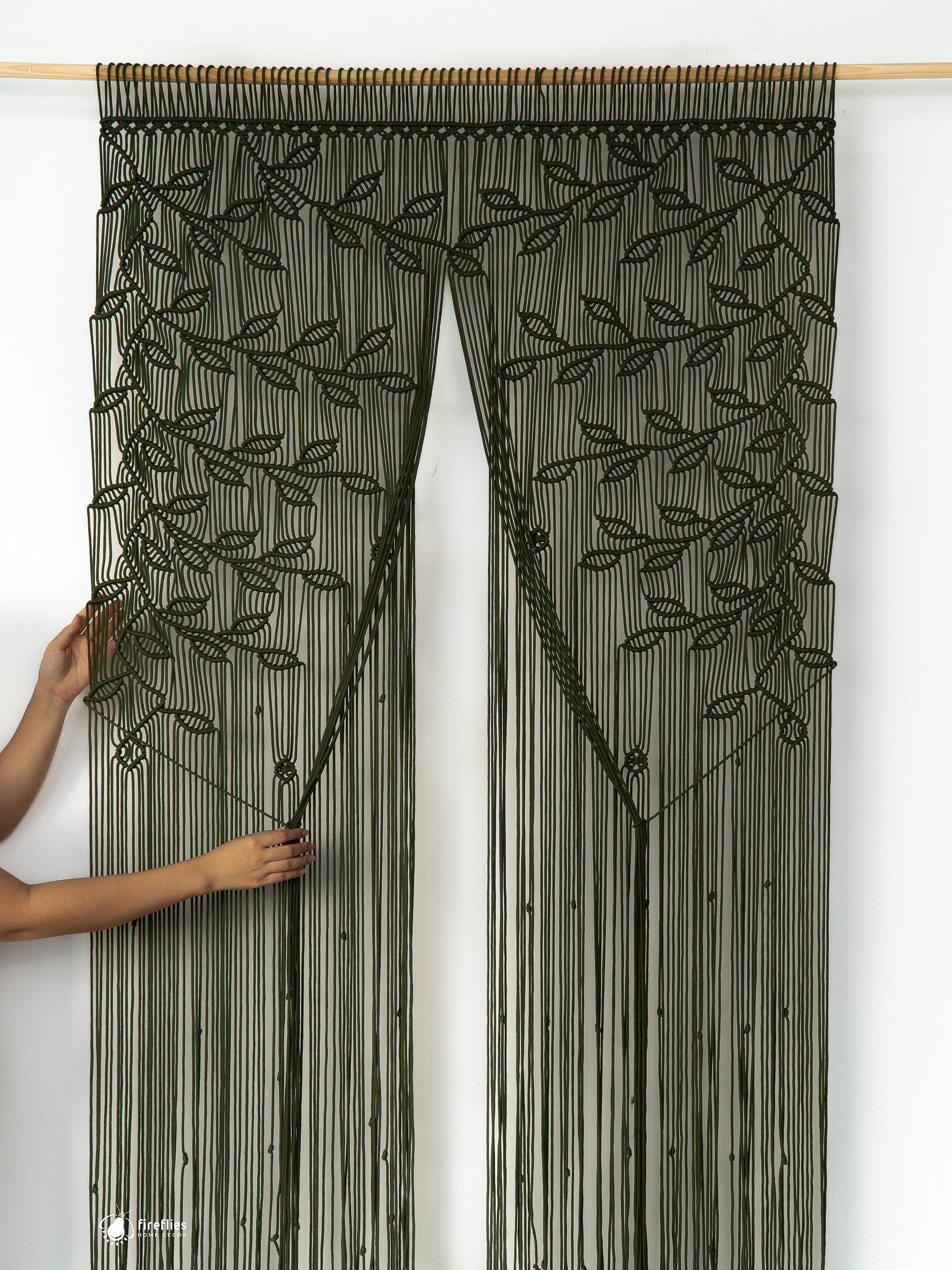 Black beaded curtain with leaf pattern held by a person against a white background