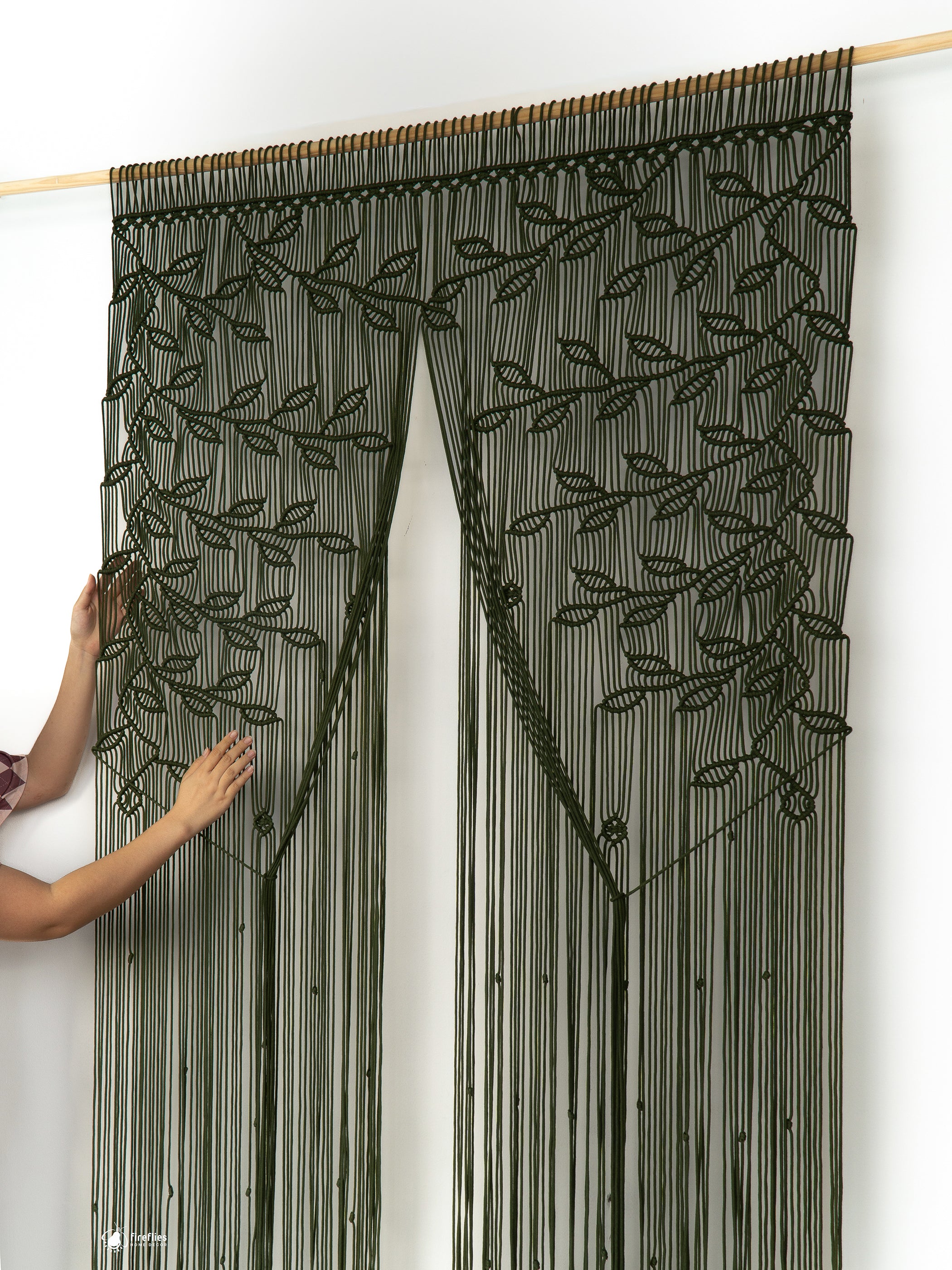Black beaded curtain with leaf pattern held by a person against a white background