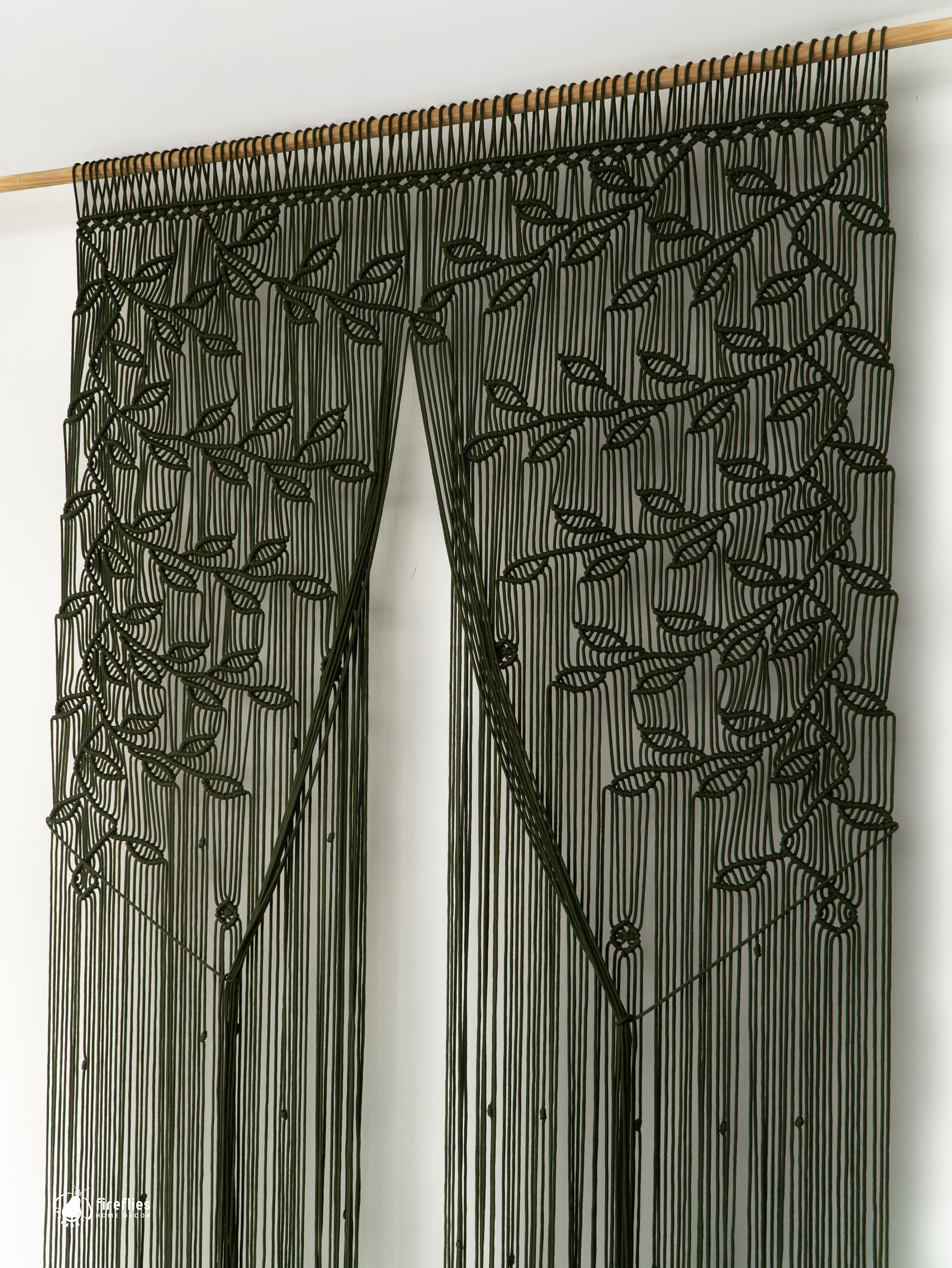 Black beaded curtain with leaf pattern on a wooden rod against a white wall