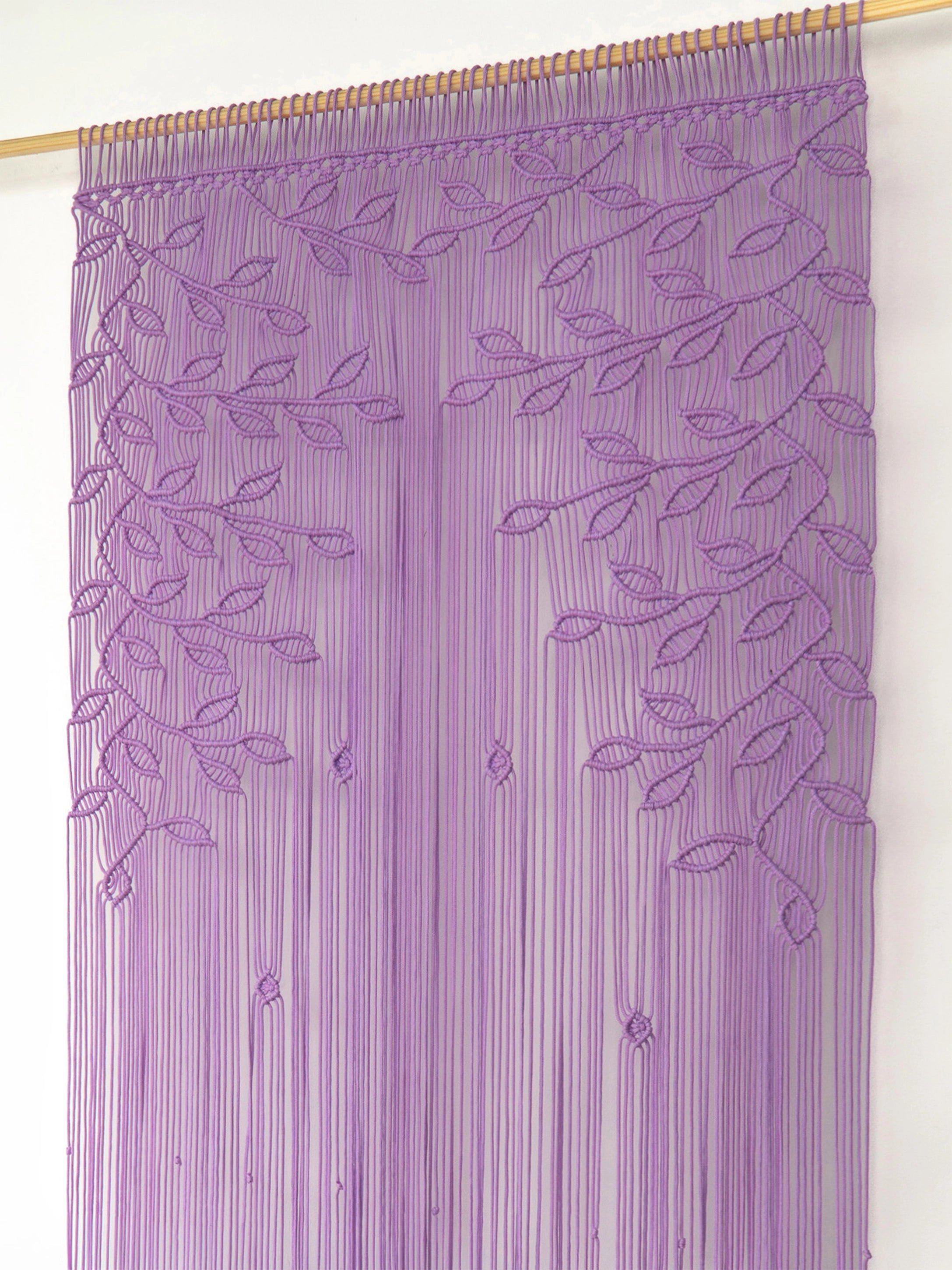 A purple beaded curtain with embroidered leaf and vine patterns, hanging from a wooden dowel against a plain white wall.