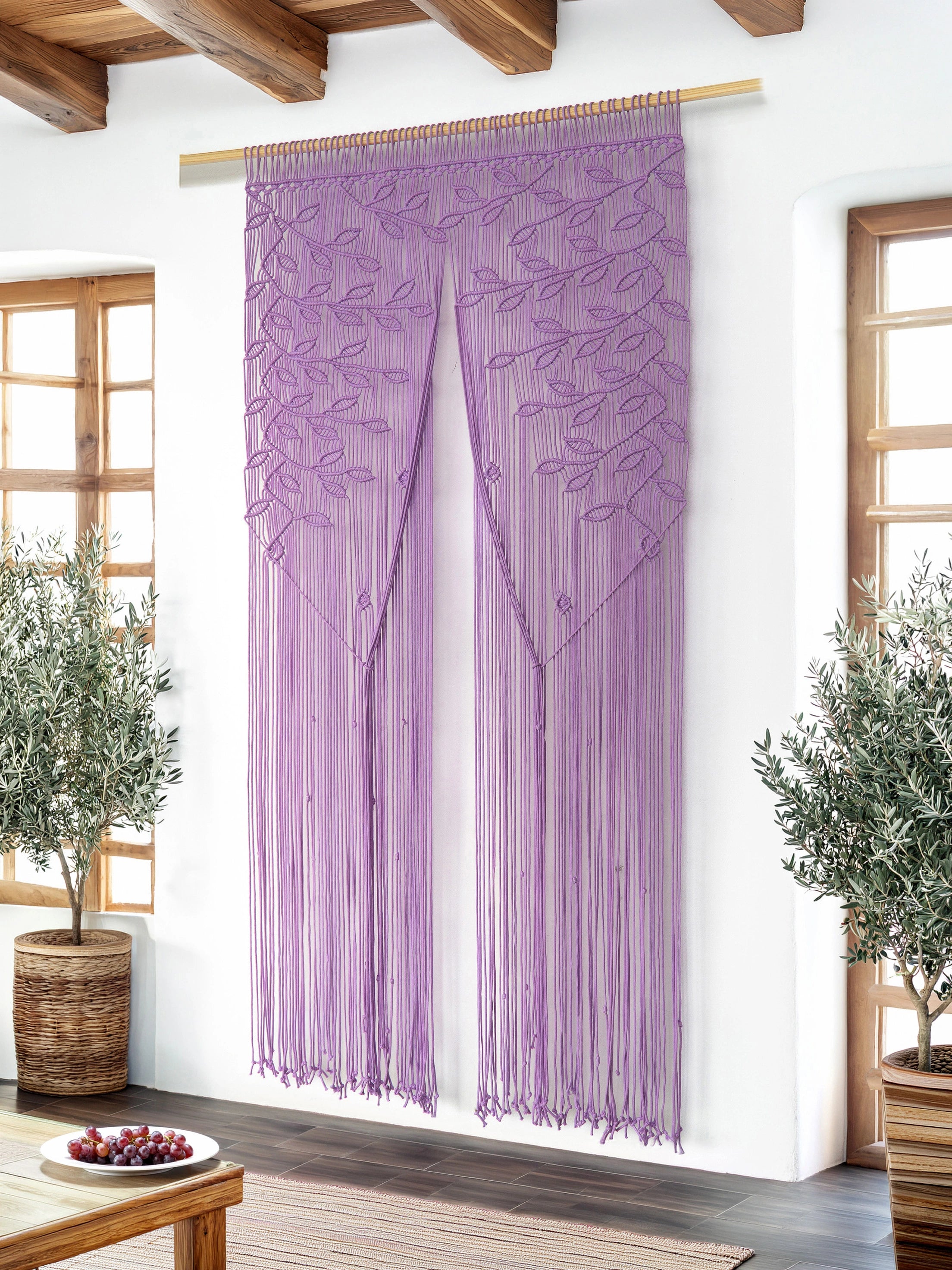 A purple beaded curtain with embroidered floral patterns hangs from a wooden rod in a bright room with white walls, wooden ceiling beams, and potted plants.