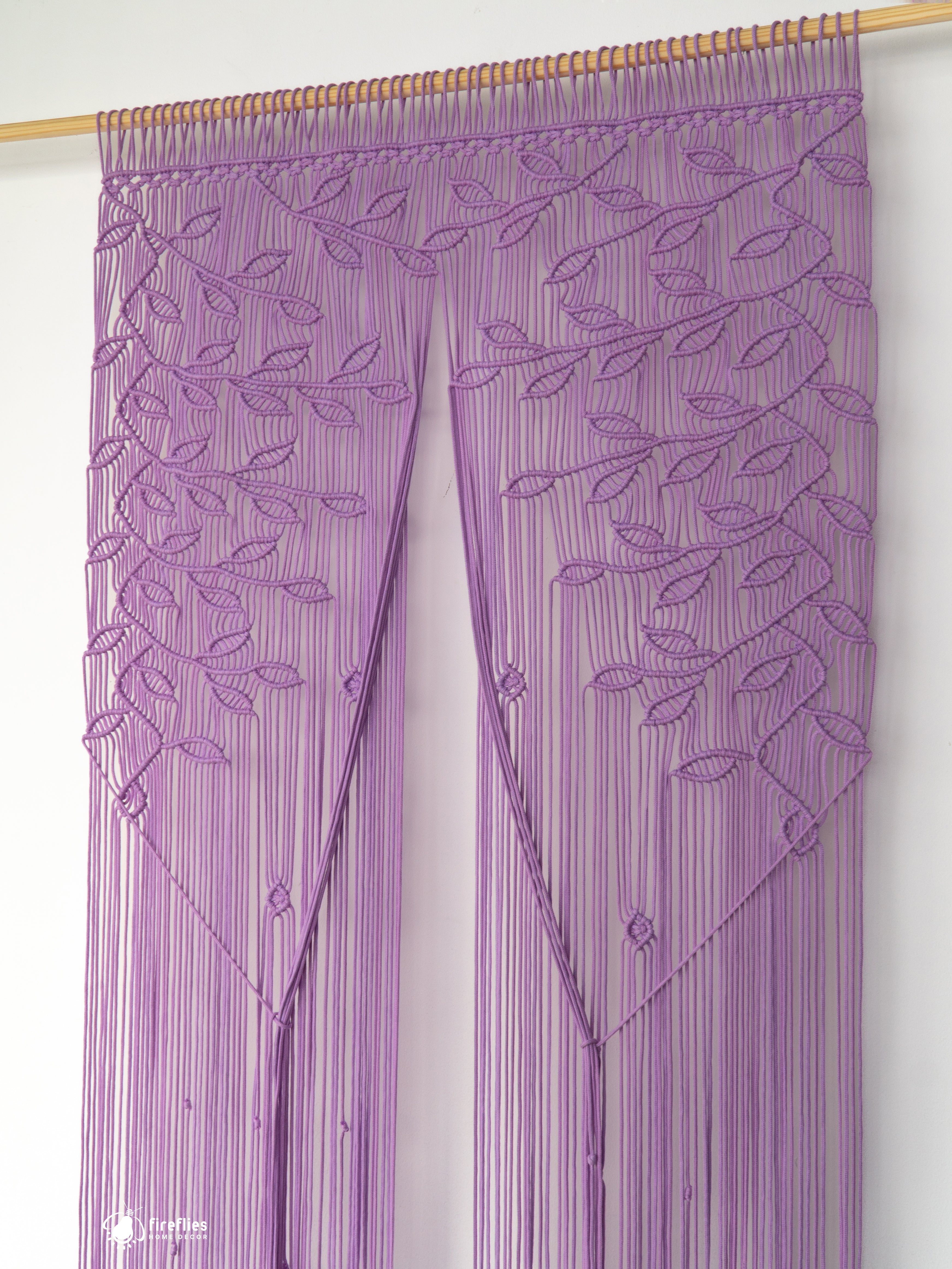 Purple string curtain with leaf pattern on a wooden rod against a white background